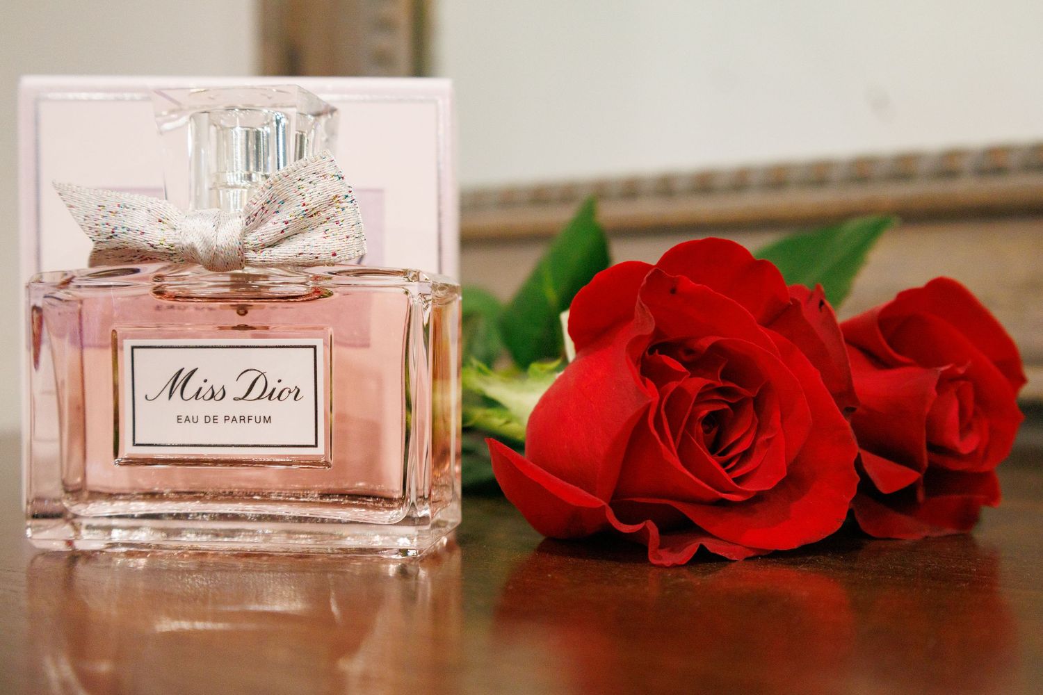 Pink perfume bottle and red roses arranged on a reflective surface.