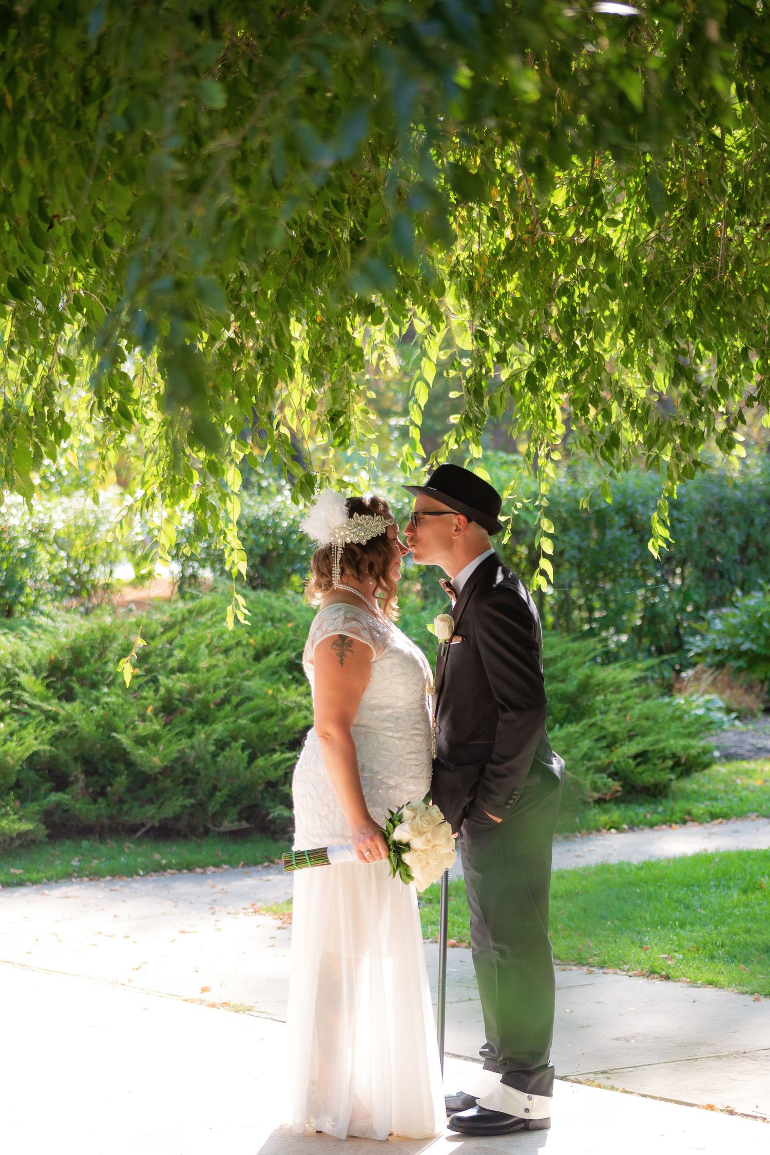 A tender wedding moment under weeping willow trees in a lush garden setting.