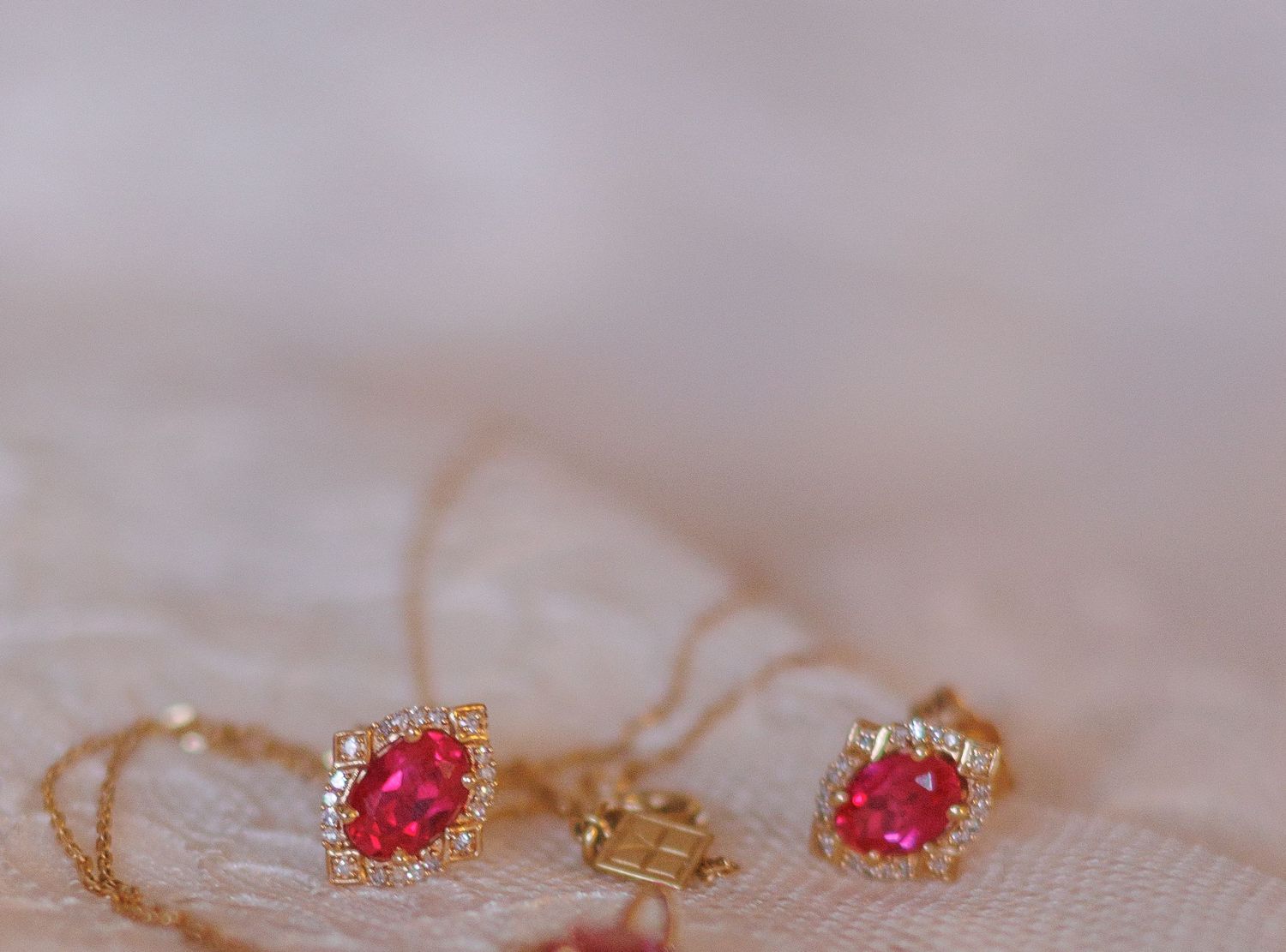 Ruby and gold earrings displayed on delicate lace fabric.