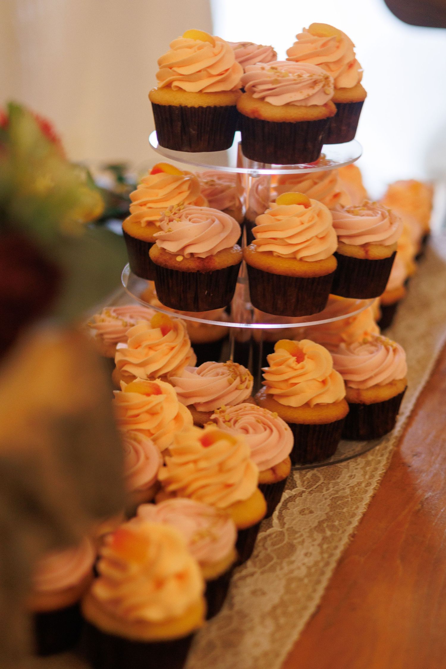 Peach-colored frosted cupcakes arranged on tiered display stand.