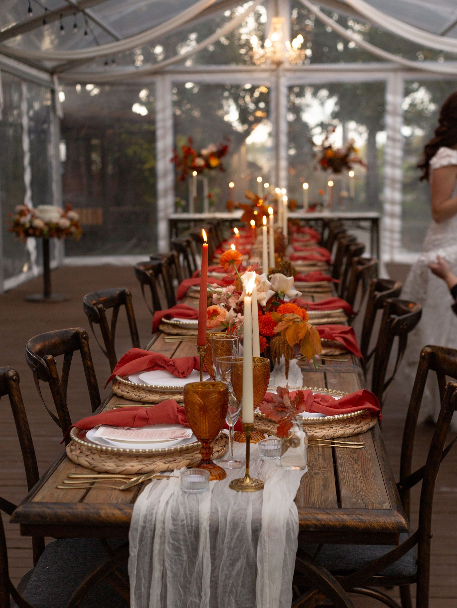 Rustic wedding reception table set with orange accents and white linens under tent.