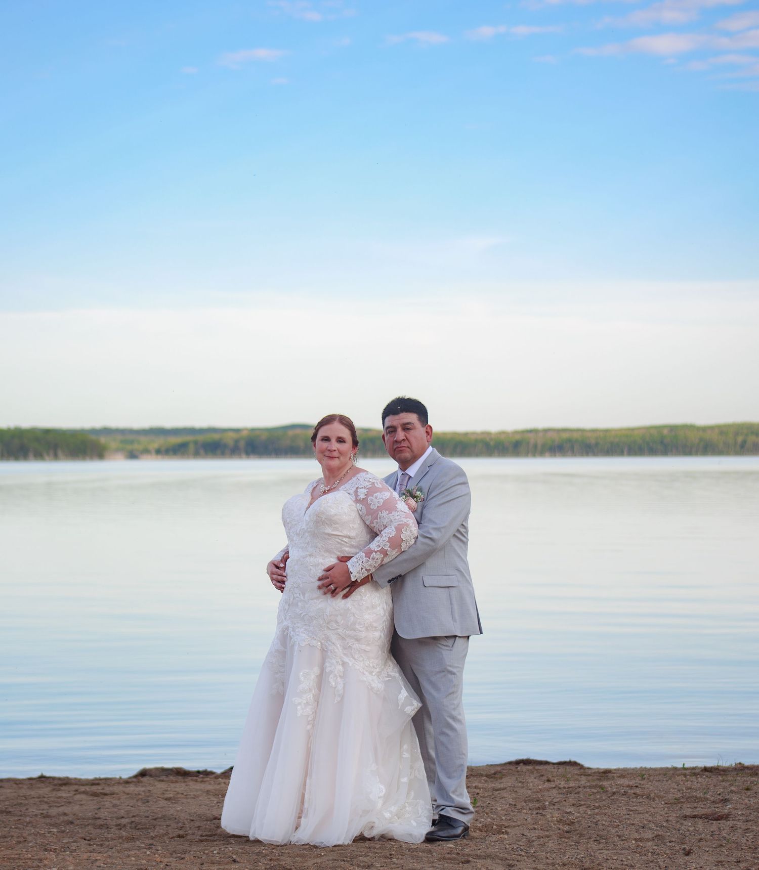 A lakeside wedding portrait with a couple in formal attire against calm waters and blue skies.