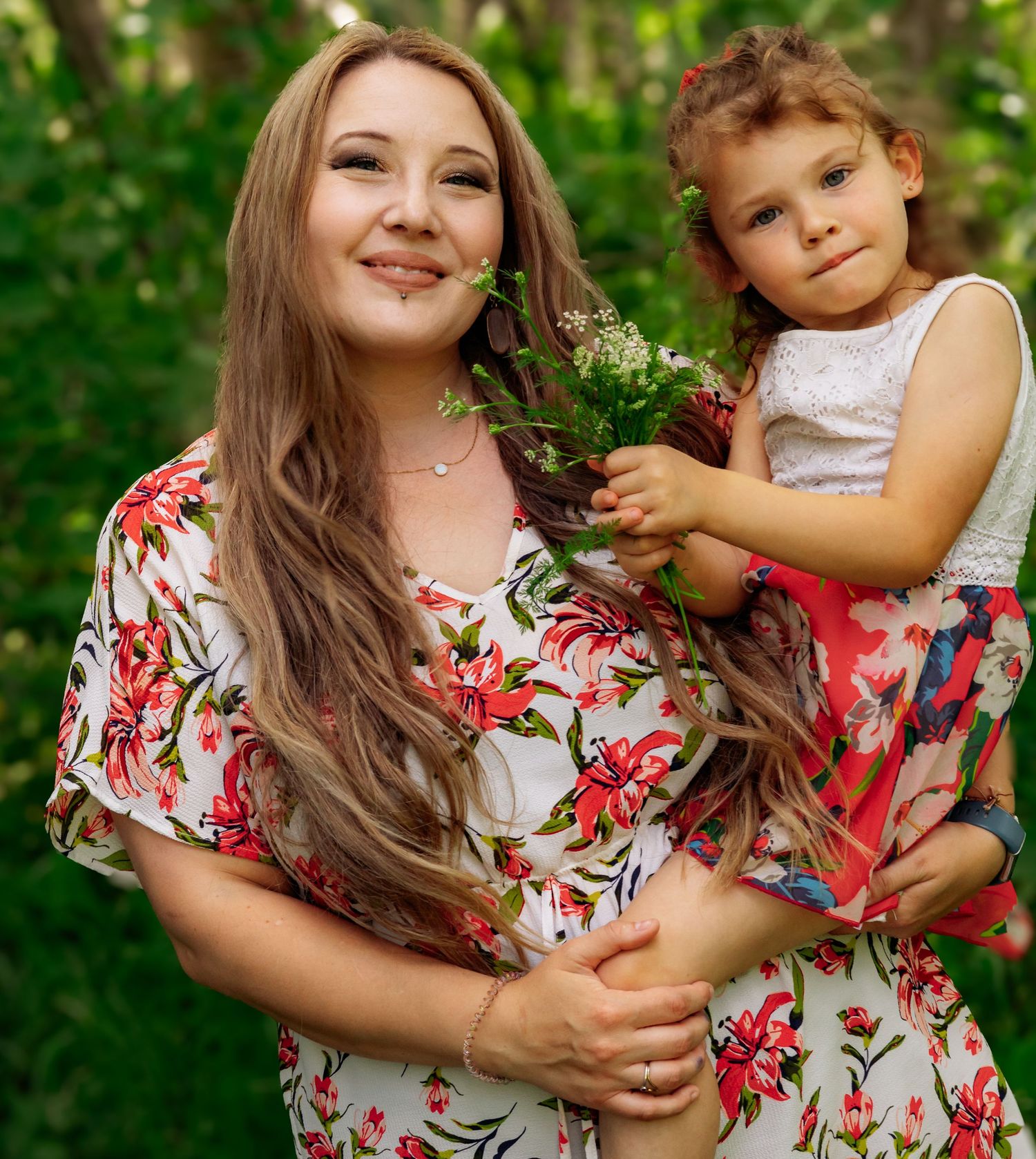 A heartwarming outdoor portrait featuring matching floral dresses against a green natural backdrop.