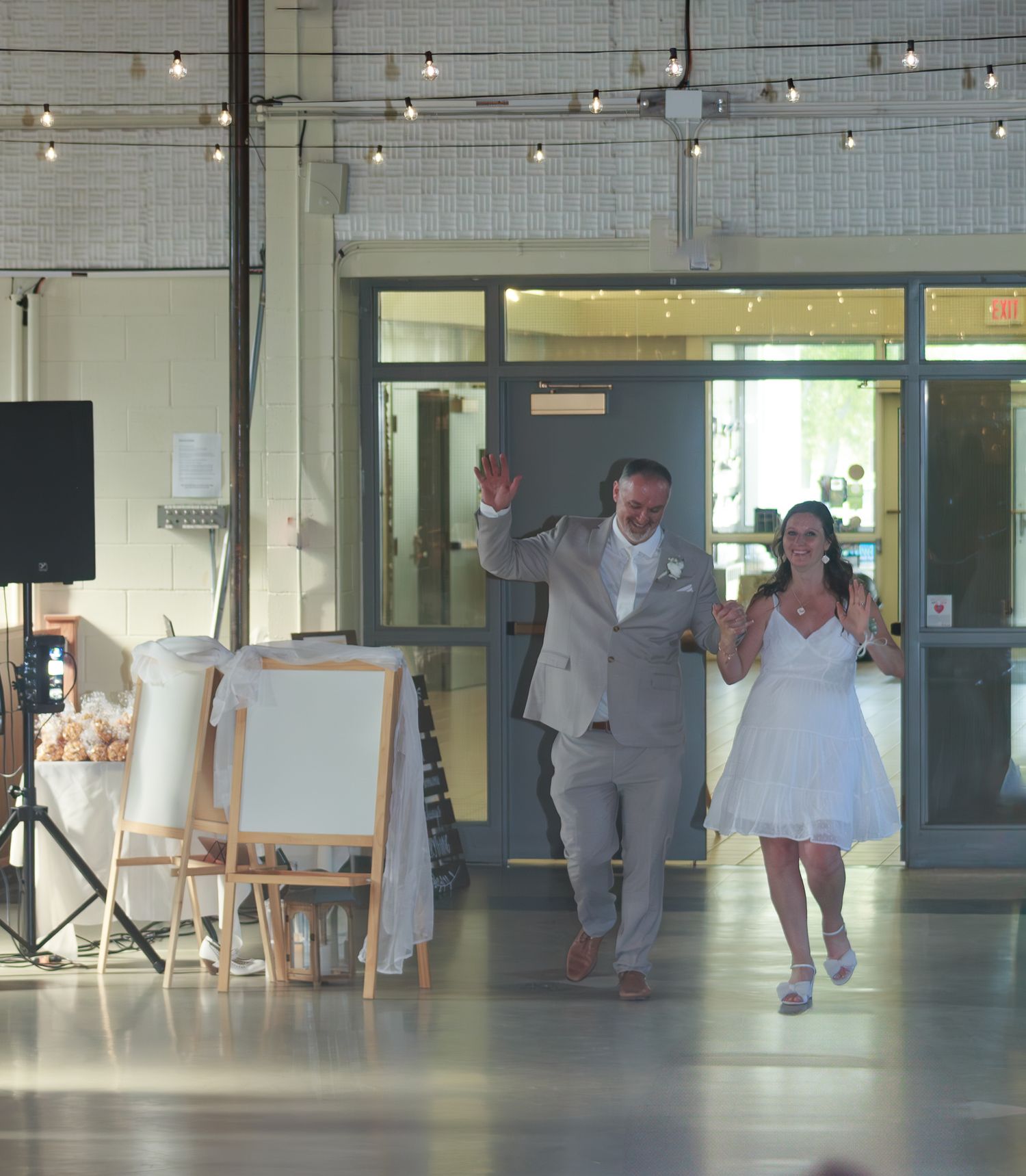 Wedding reception venue with string lights and people dancing on an indoor floor.