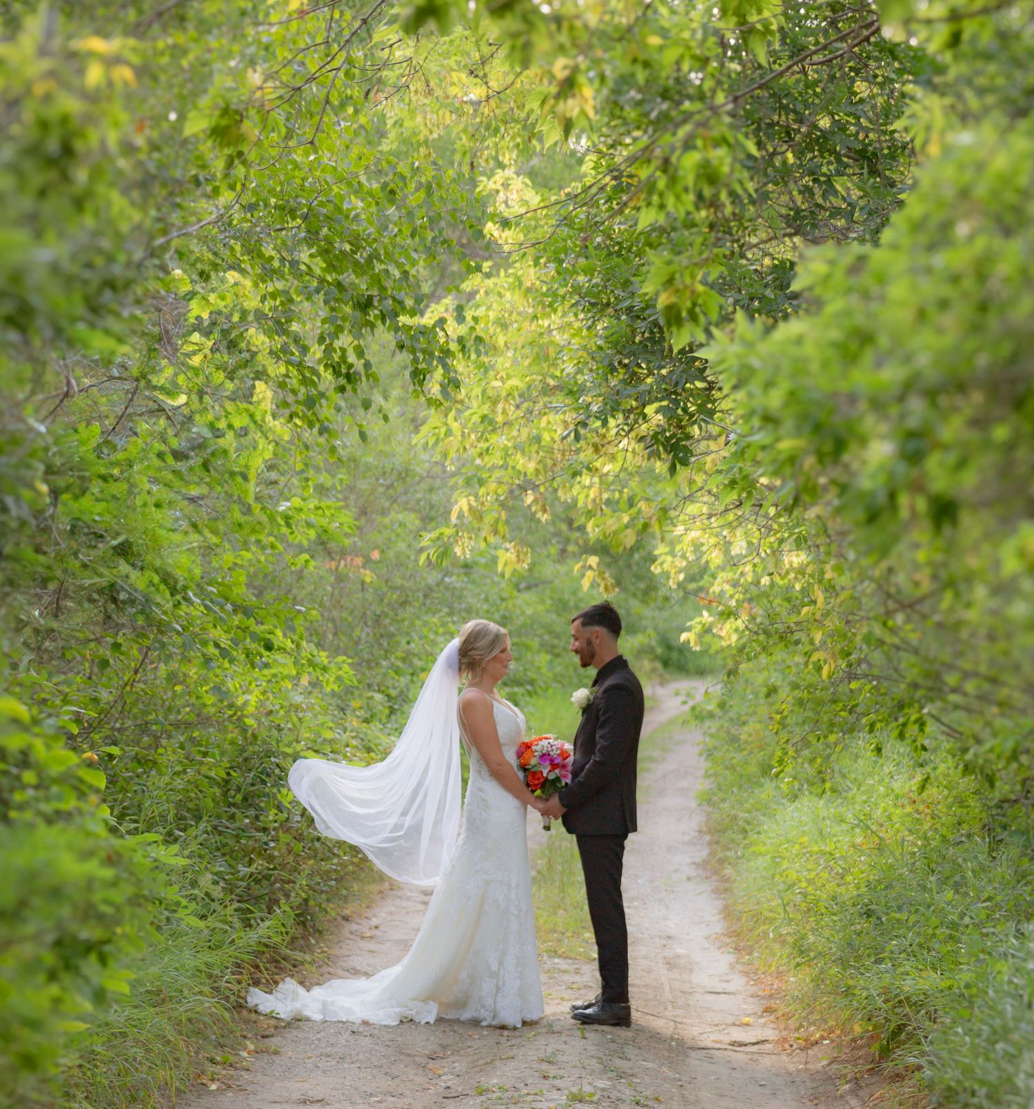 Wedding couple sharing intimate moments on a tree-lined nature path.
