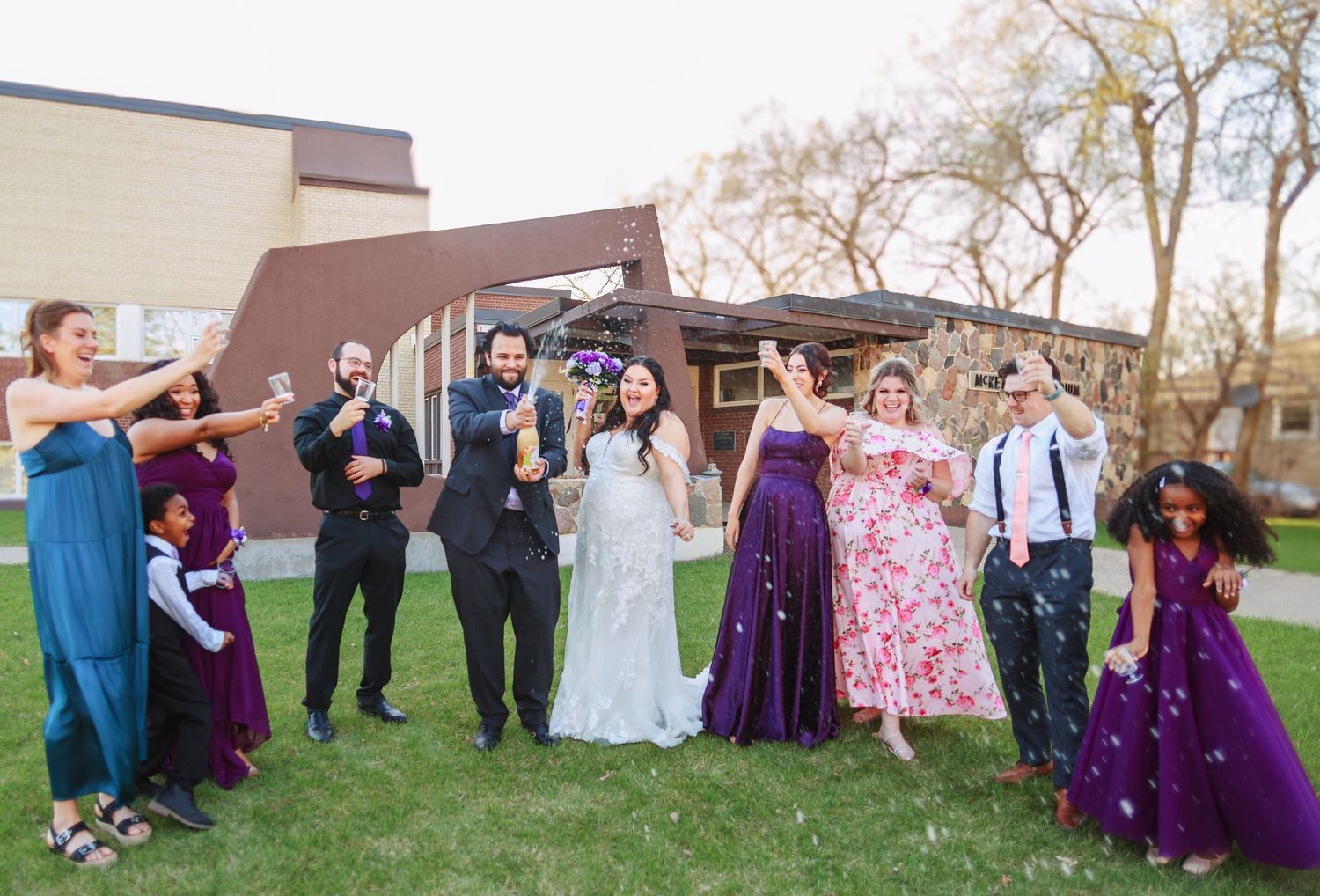 Wedding party striking playful poses outdoors with bridesmaids in purple gowns.