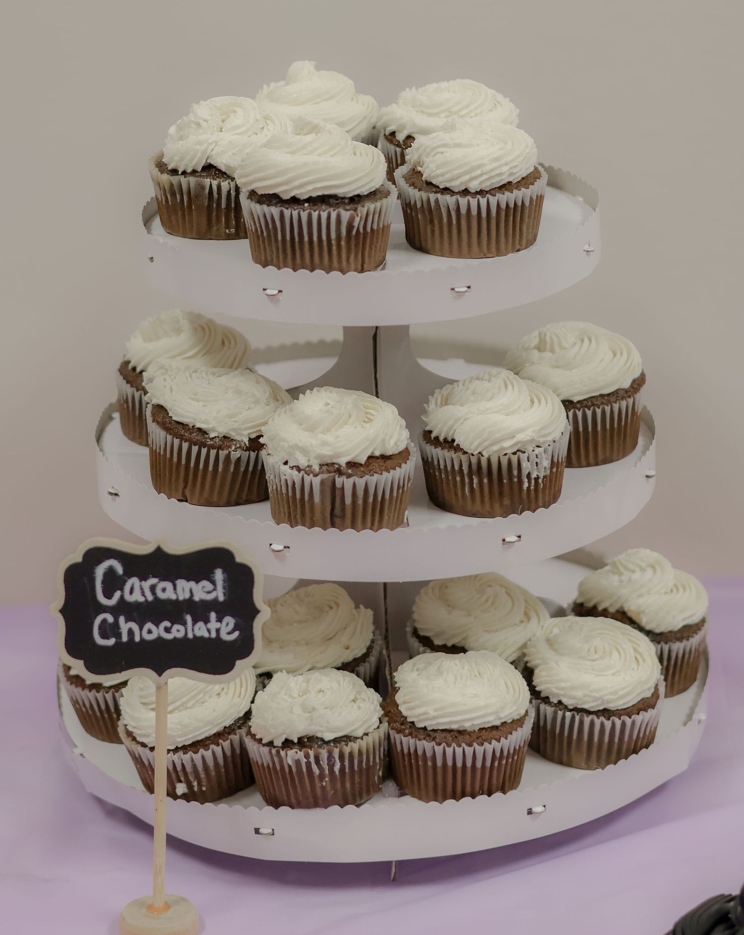 Multi-tiered display of chocolate cupcakes with white frosting and chalkboard flavor labels.