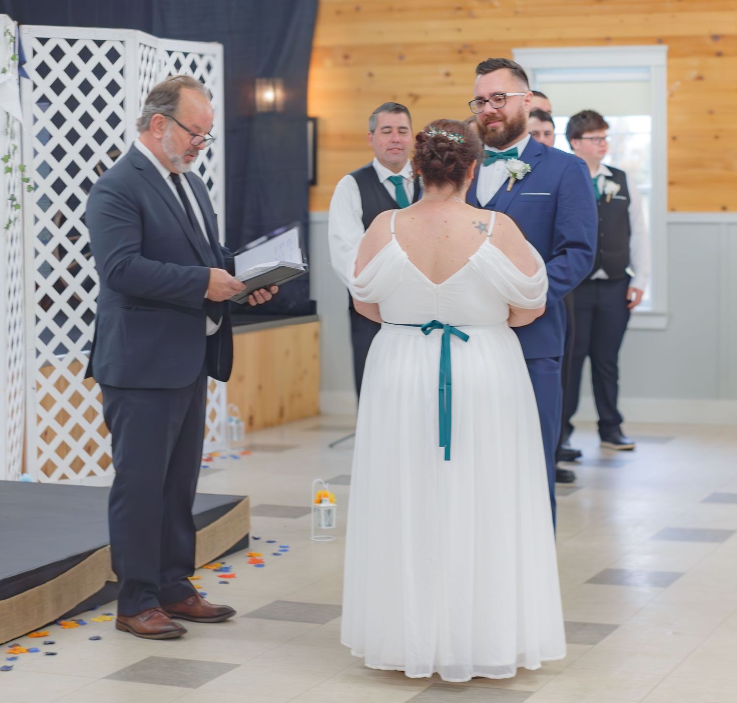 Wedding ceremony taking place in a rustic wooden venue with white lattice decorations.