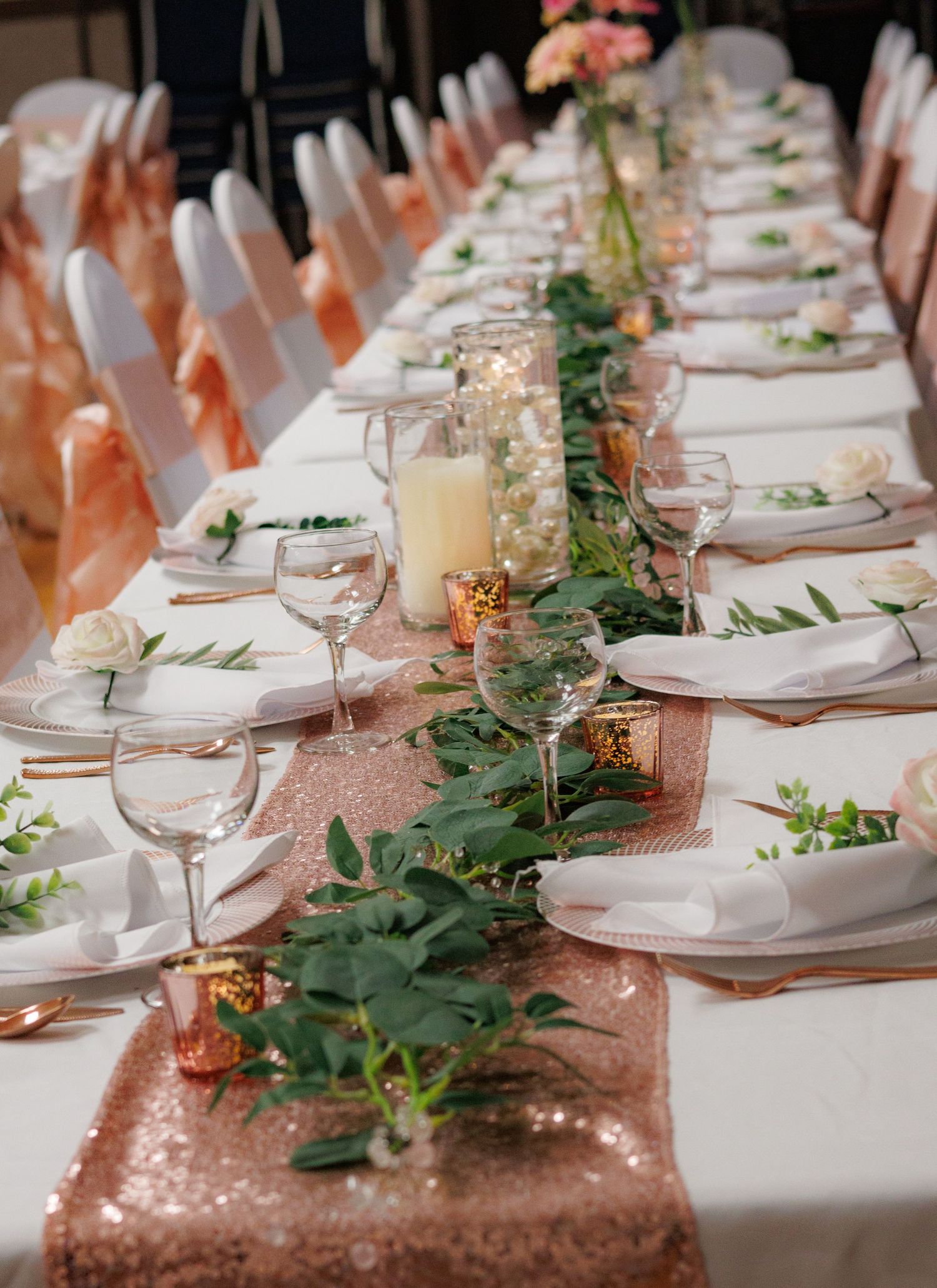 Wedding table setup with rose gold sequin runner and green foliage decorations.