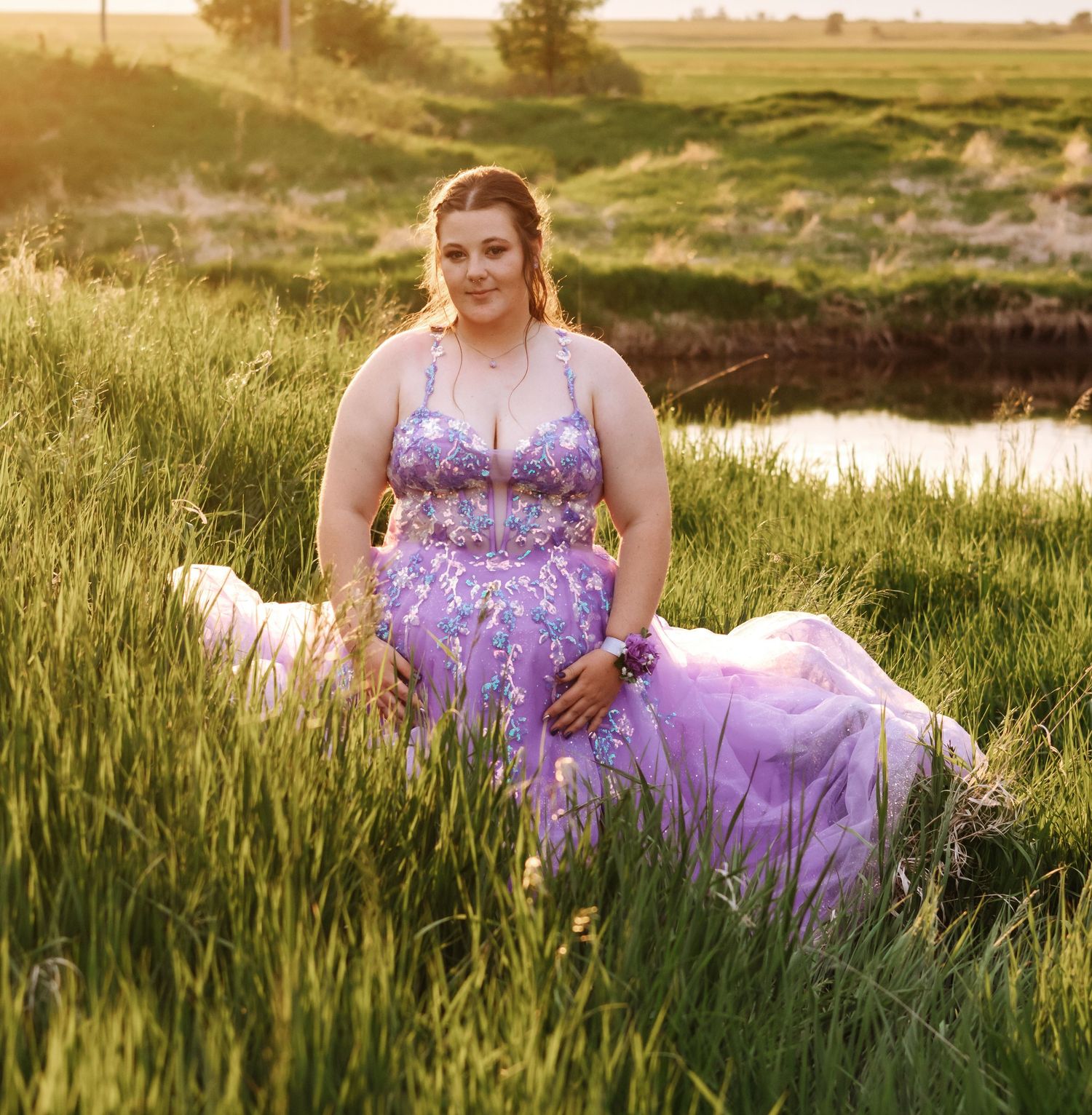 Purple ballgown glows in golden light amidst tall grass at sunset.