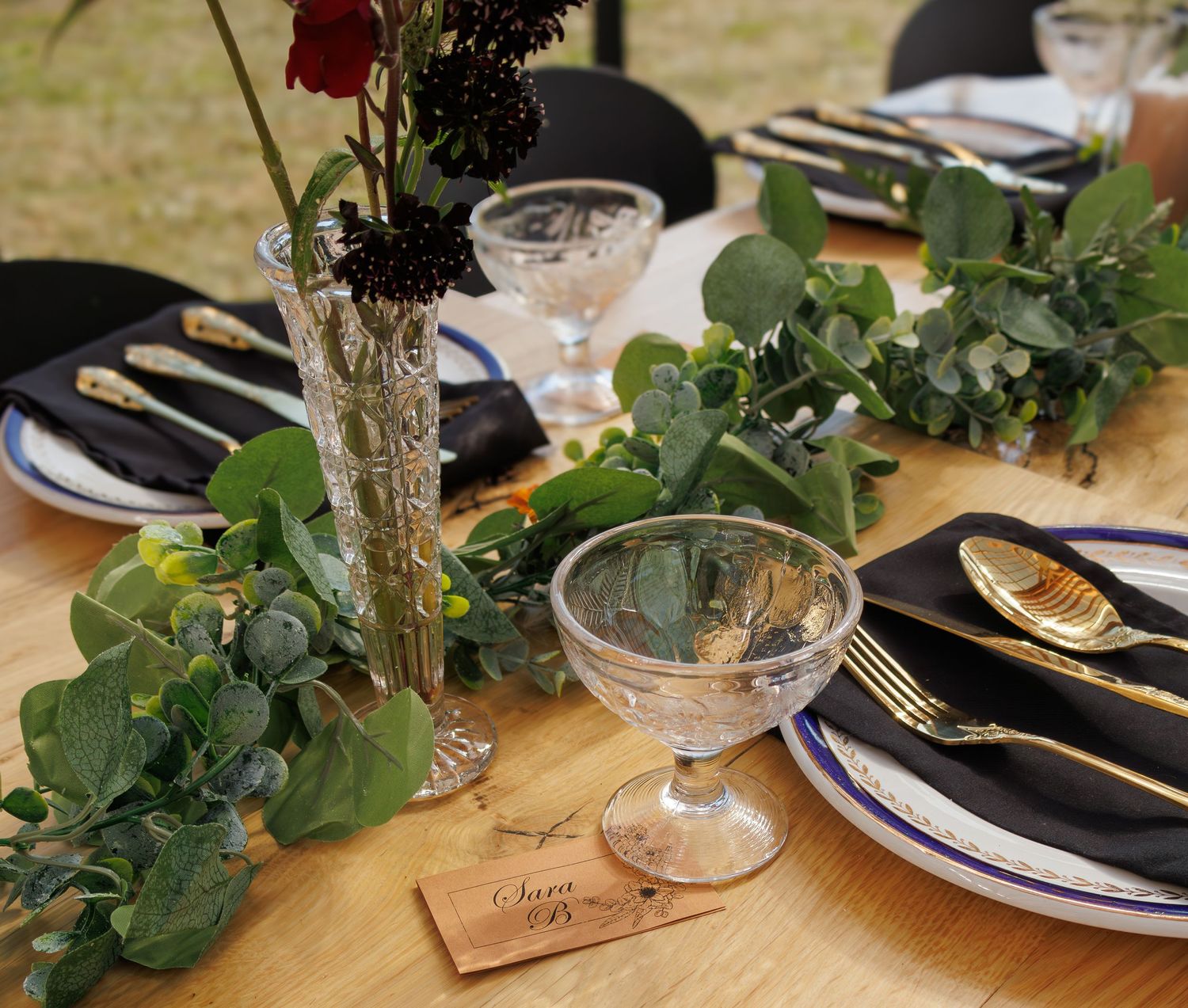Elegant table settings with greenery and black napkins at a rustic reception.