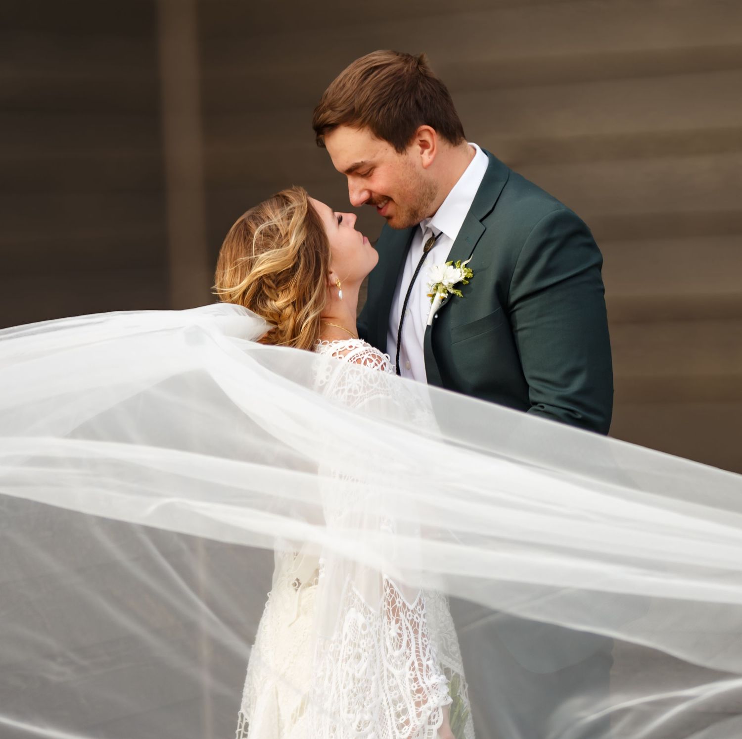 A romantic wedding portrait with flowing veil movement against a dramatic indoor backdrop.
