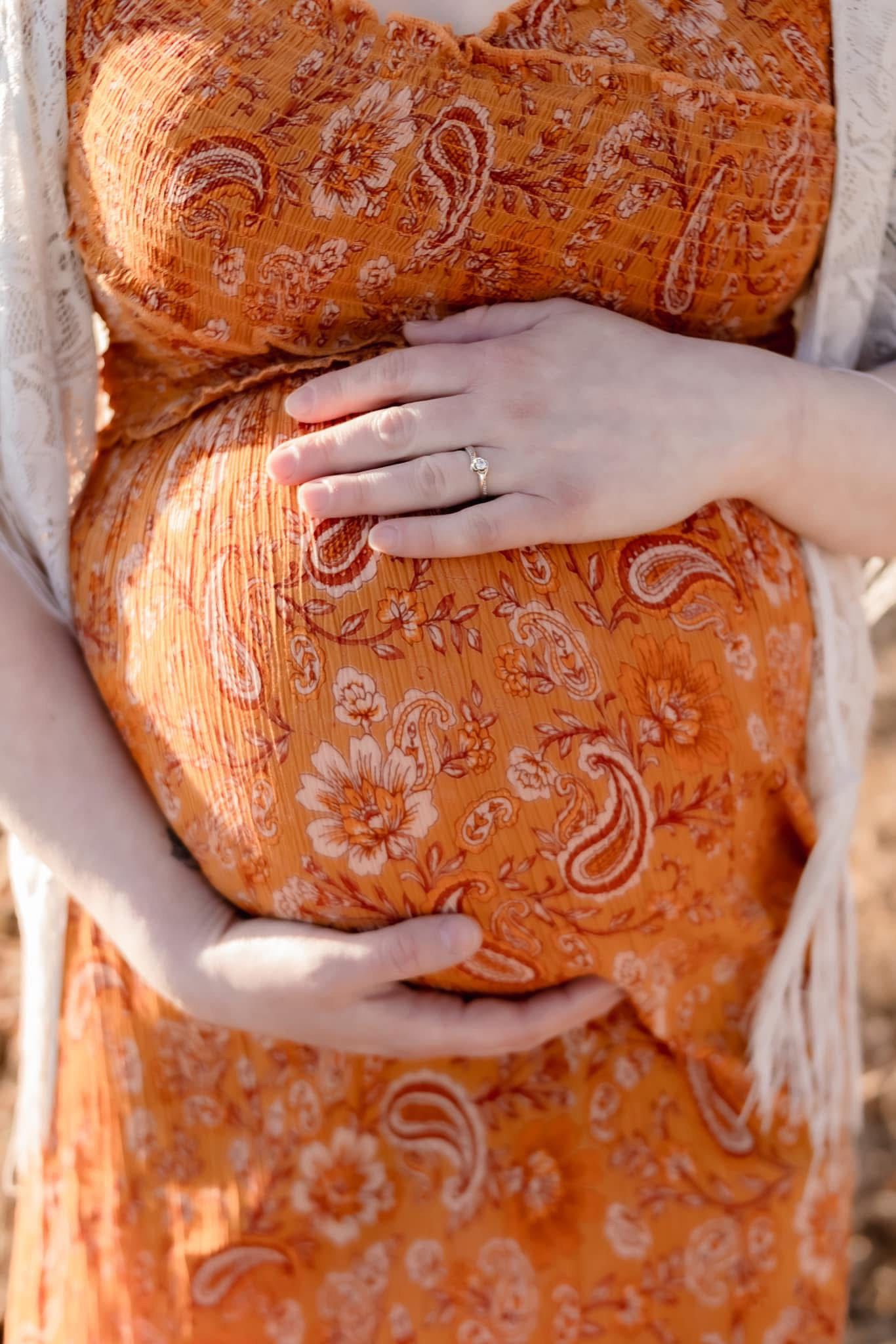 Close-up of hands cradling a baby bump in an orange paisley patterned dress.