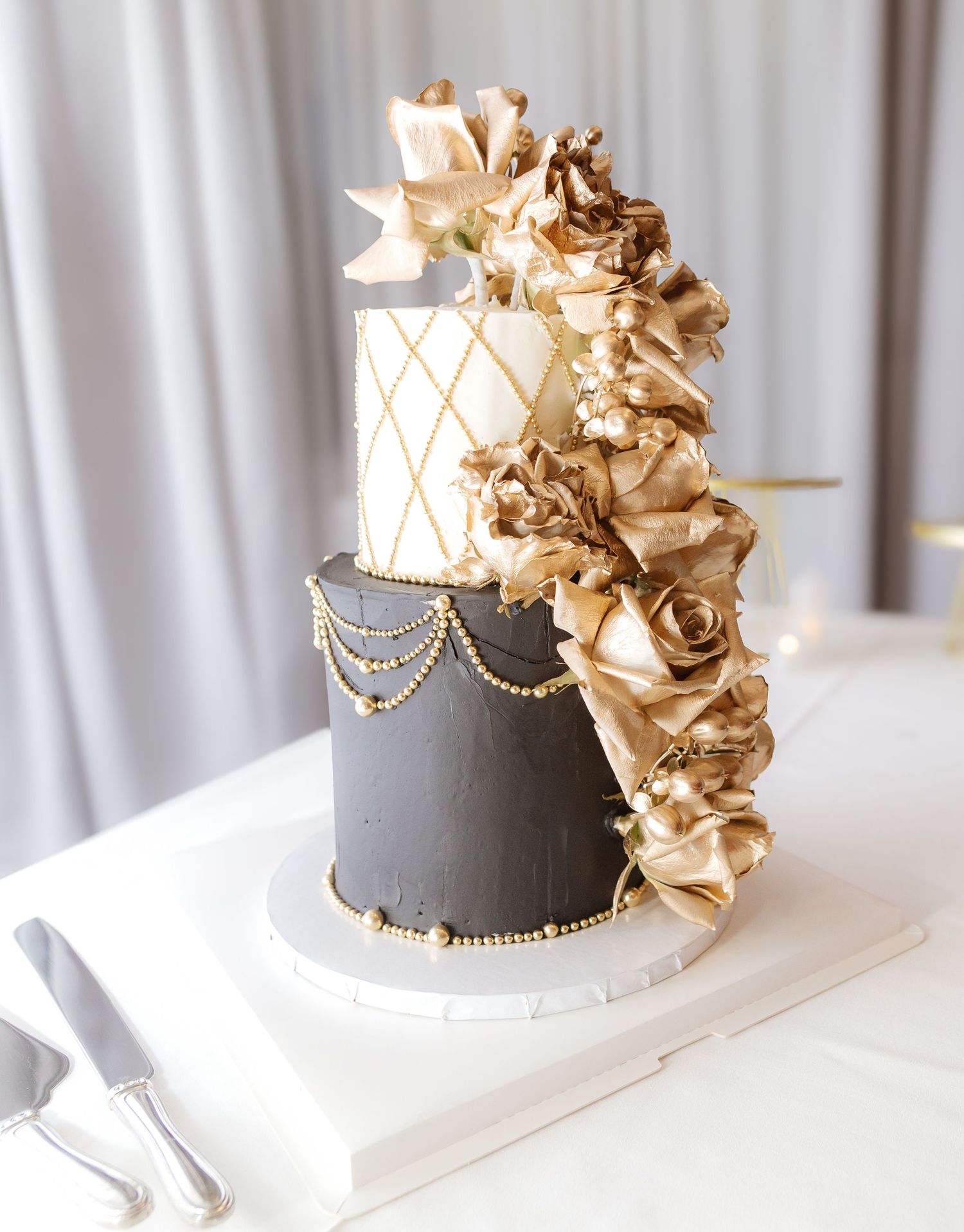 Elegant grey and gold wedding cake with ruffled details and pearl accents on white tablecloth.