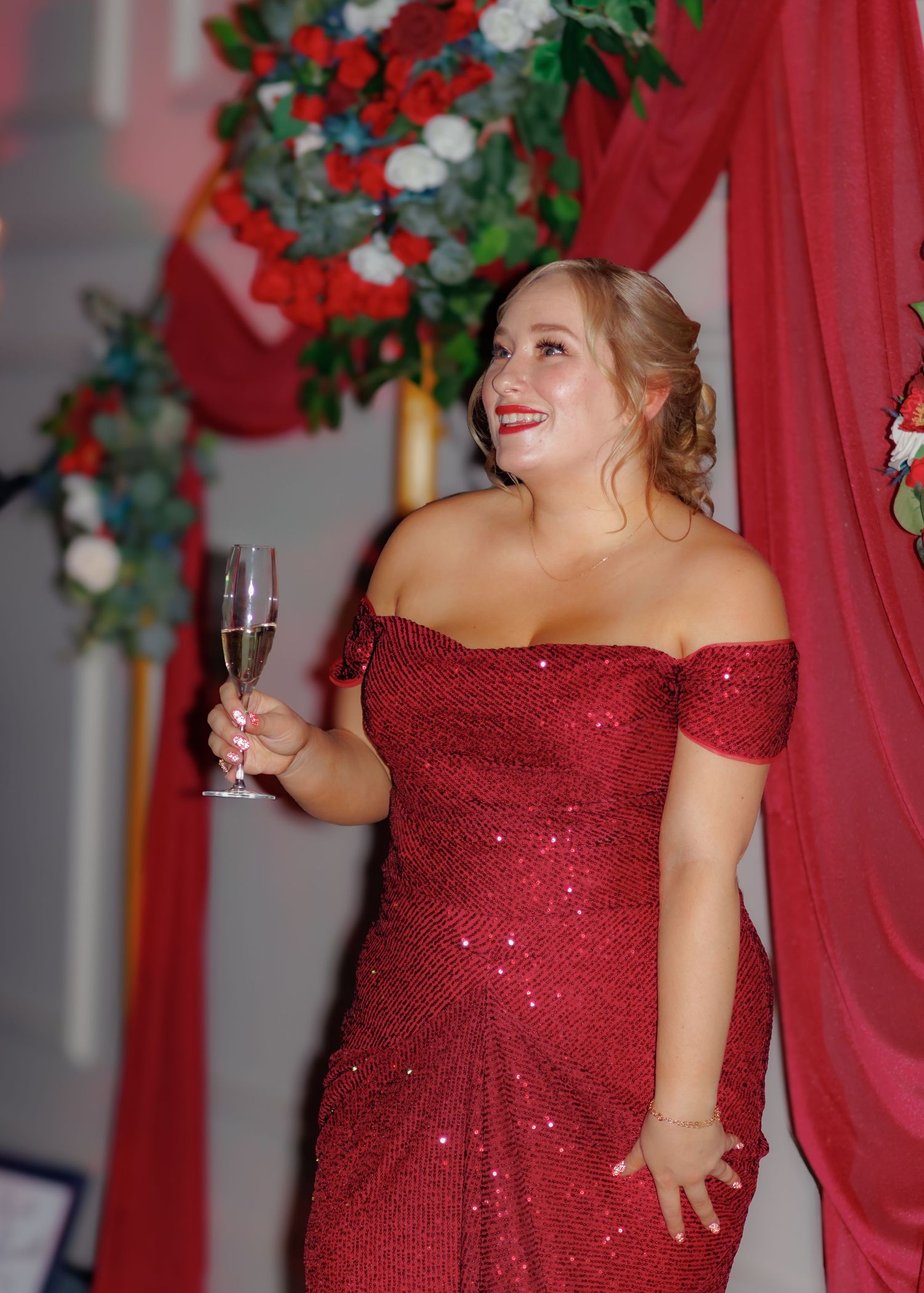 Woman in sparkling red formal dress holding champagne glass at elegant event.