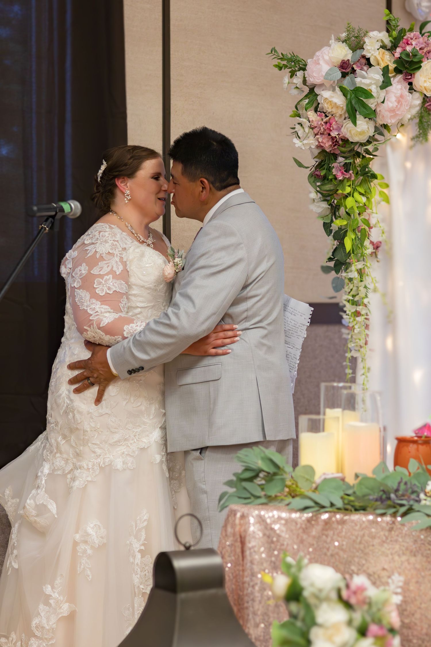 A romantic first kiss as newlyweds under a floral arch with candlelit decor.
