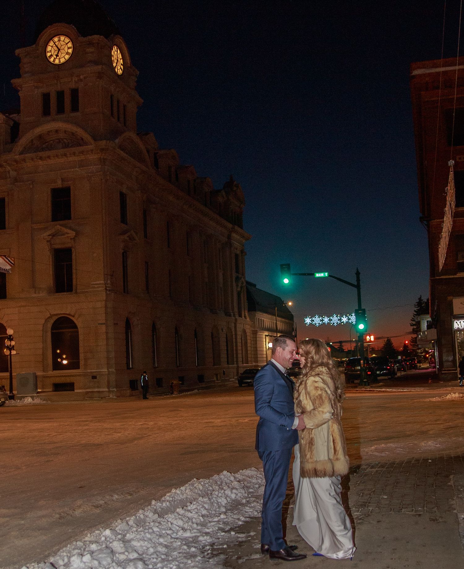 A winter wedding photo at night in front of a historic building with illuminated clock tower.