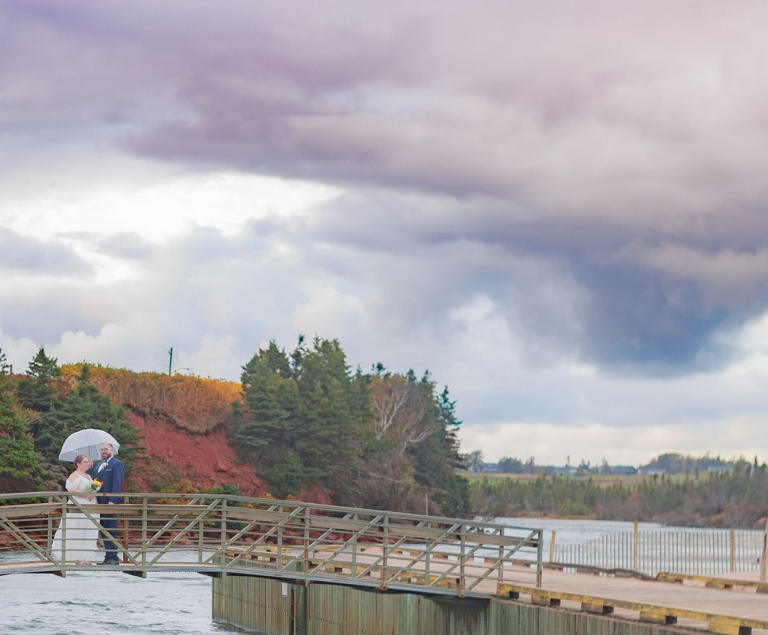 Scenic beach wedding venue with wooden dock and dramatic cloudy skies over the water.