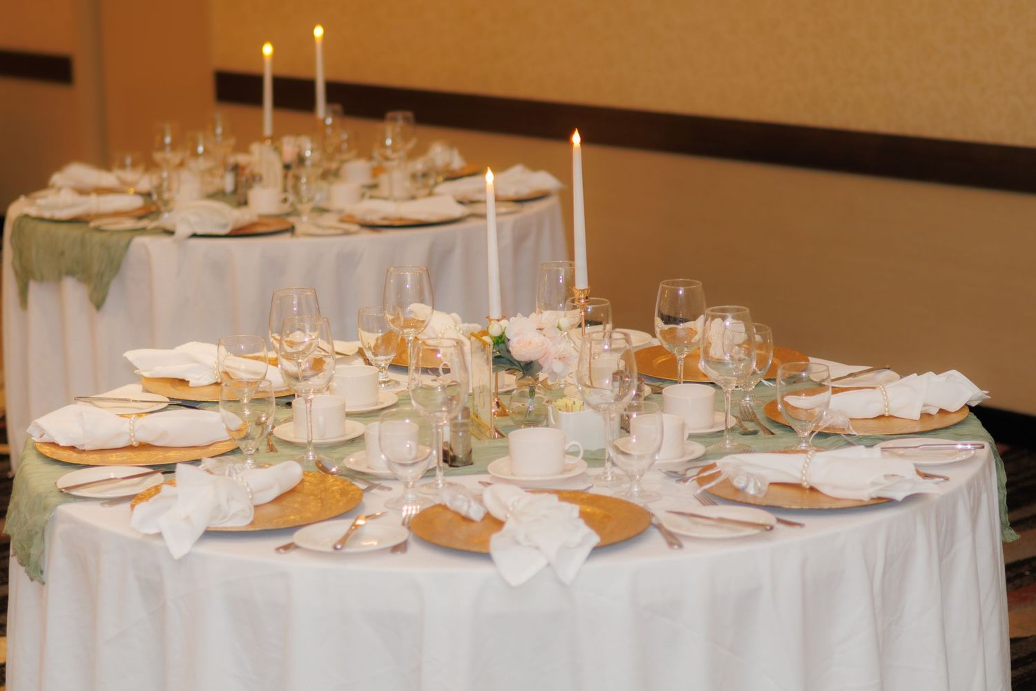 Formal round dining tables set with white linens and gold accents for an elegant reception.