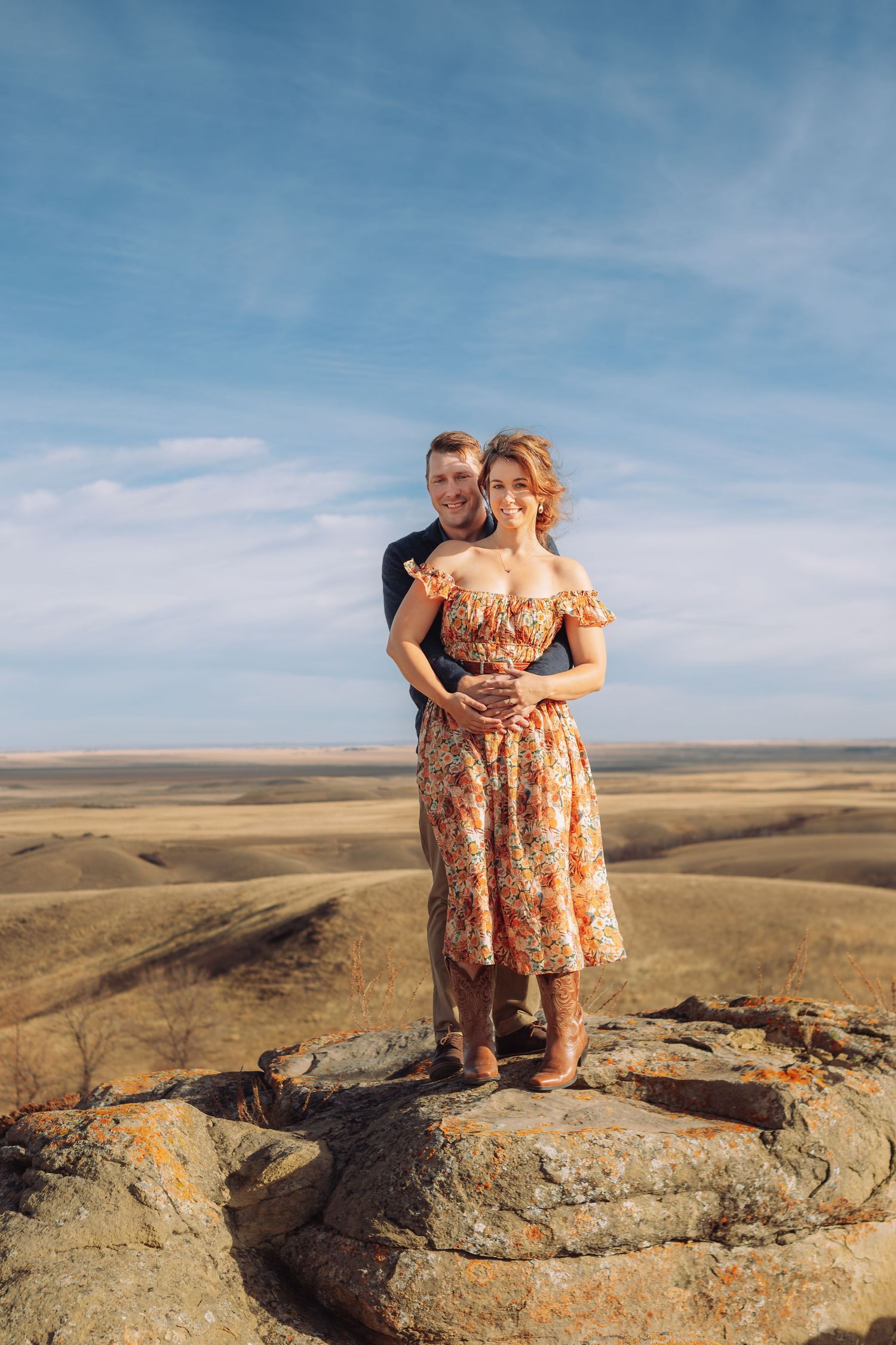 Couple standing on rocky outcrop overlooking expansive prairie landscape.