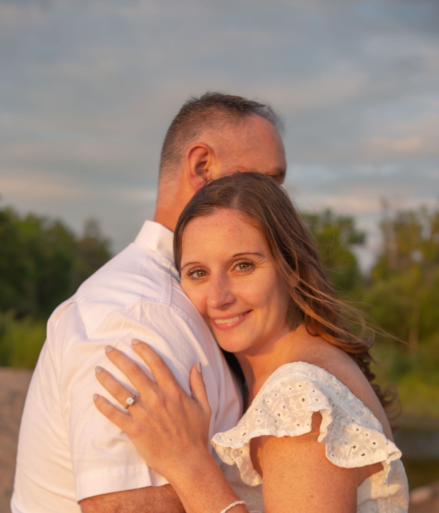 Romantic couple in white clothing embracing during golden hour photo session.