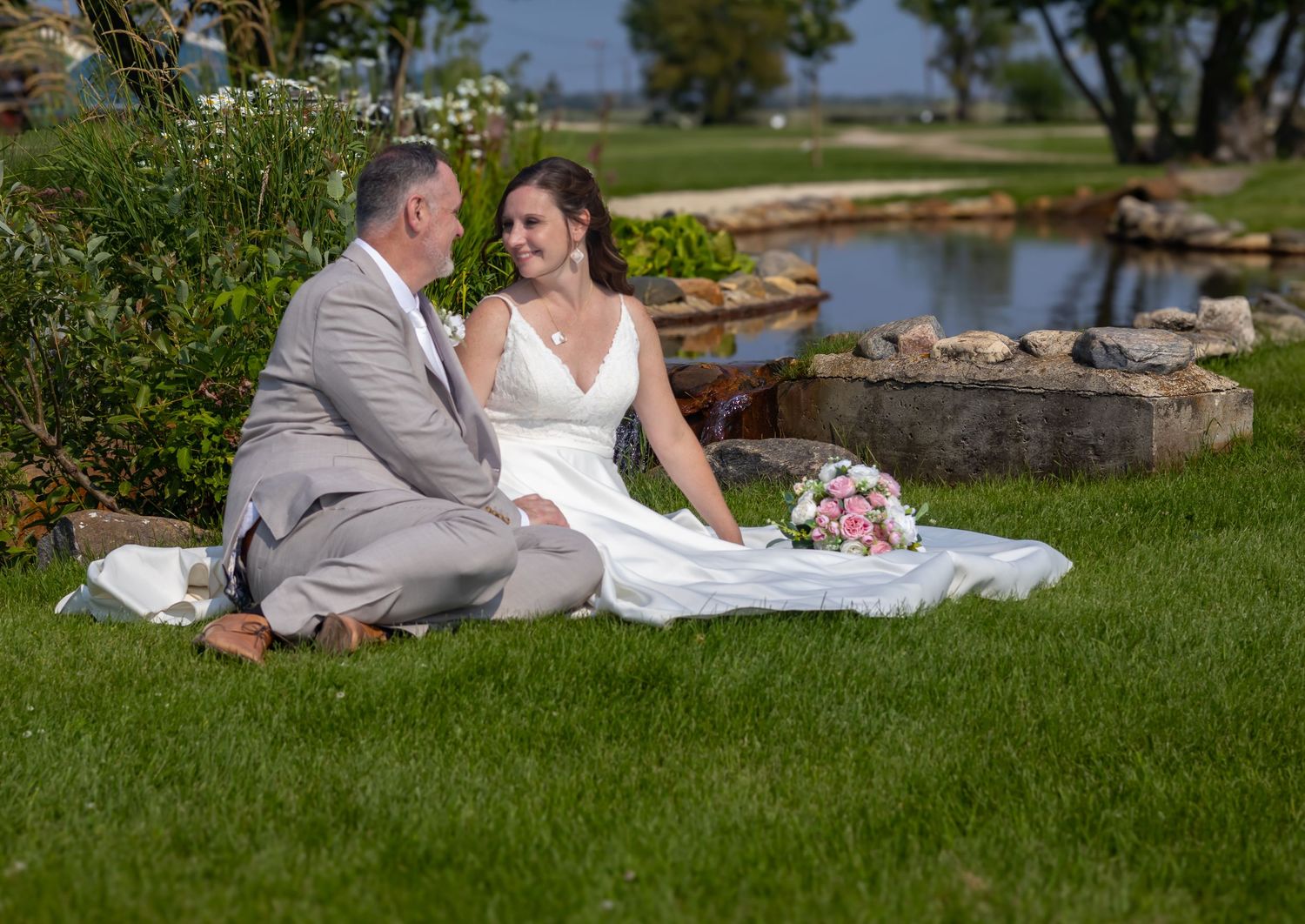 Wedding couple relaxing on manicured lawn near waterfront.