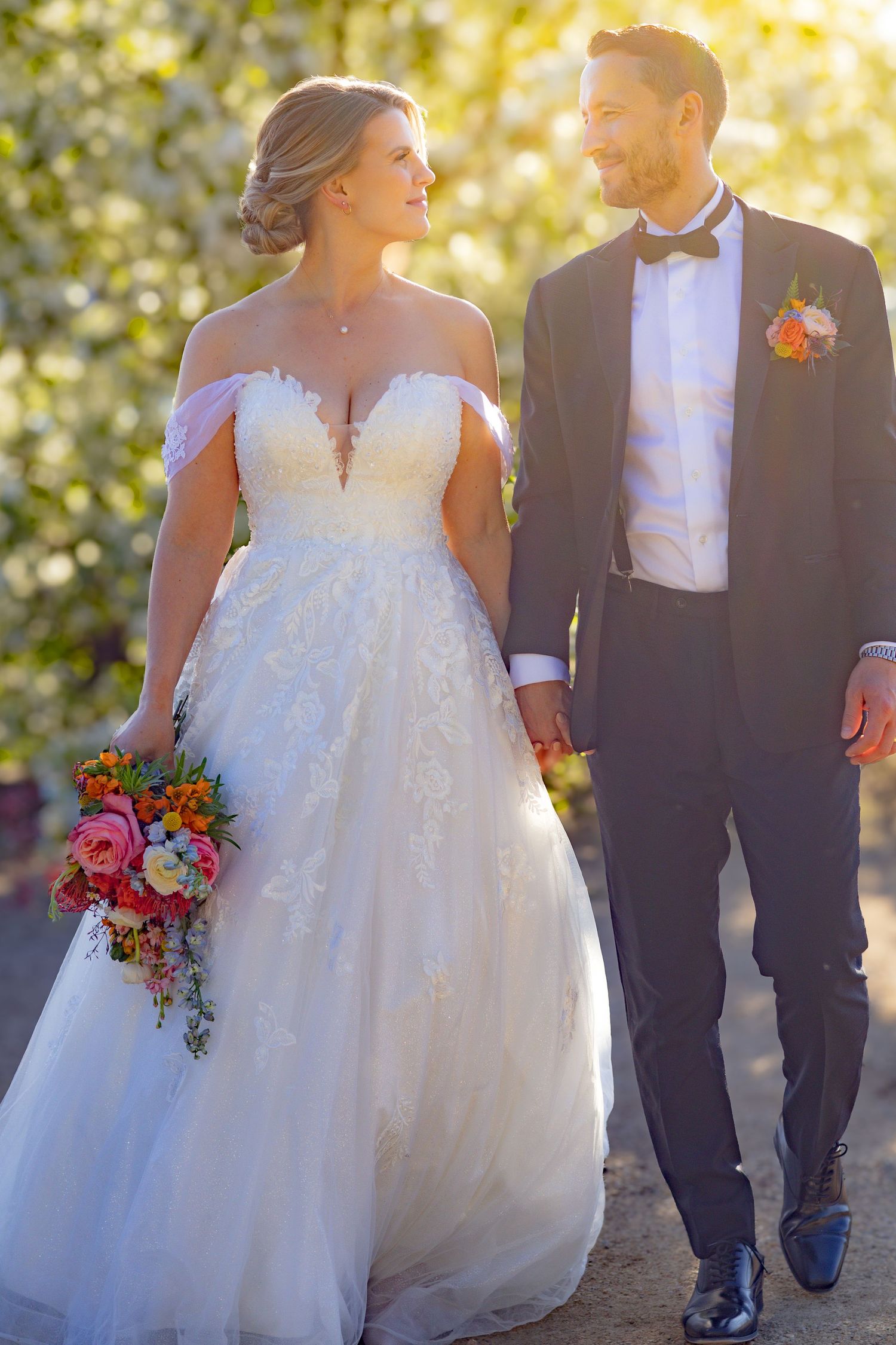 Wedding couple walking together on a path surrounded by autumn foliage.