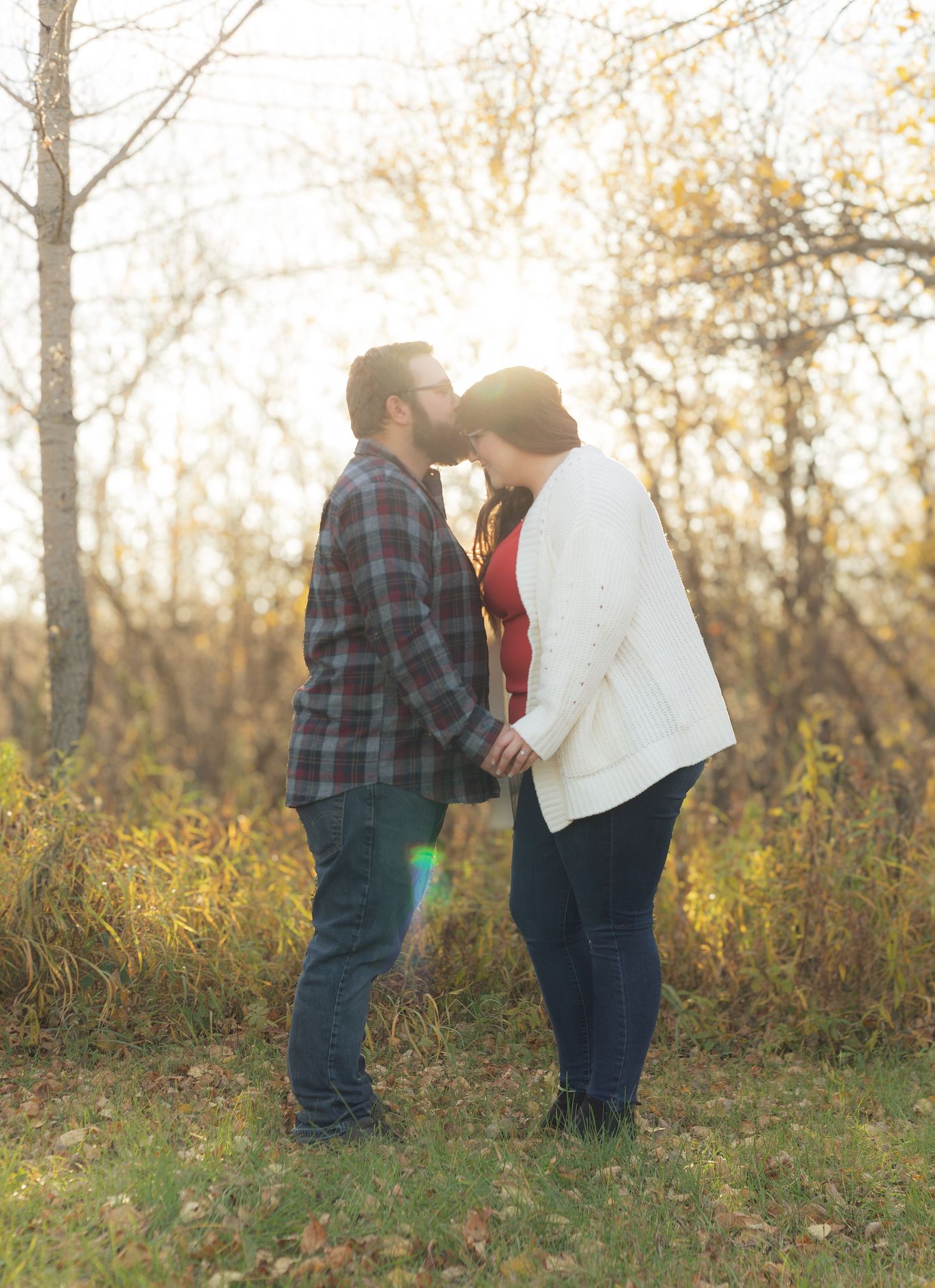 Romantic couple poses among bare trees during golden hour in autumn.