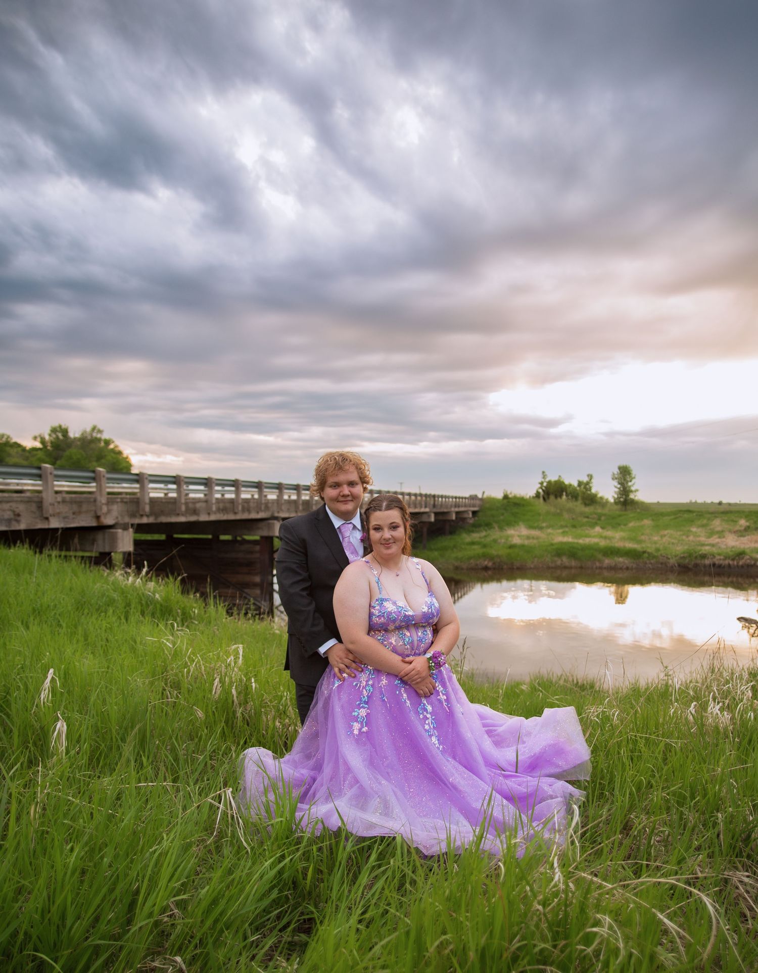 Purple dress flowing in the breeze near a wooden bridge at sunset.