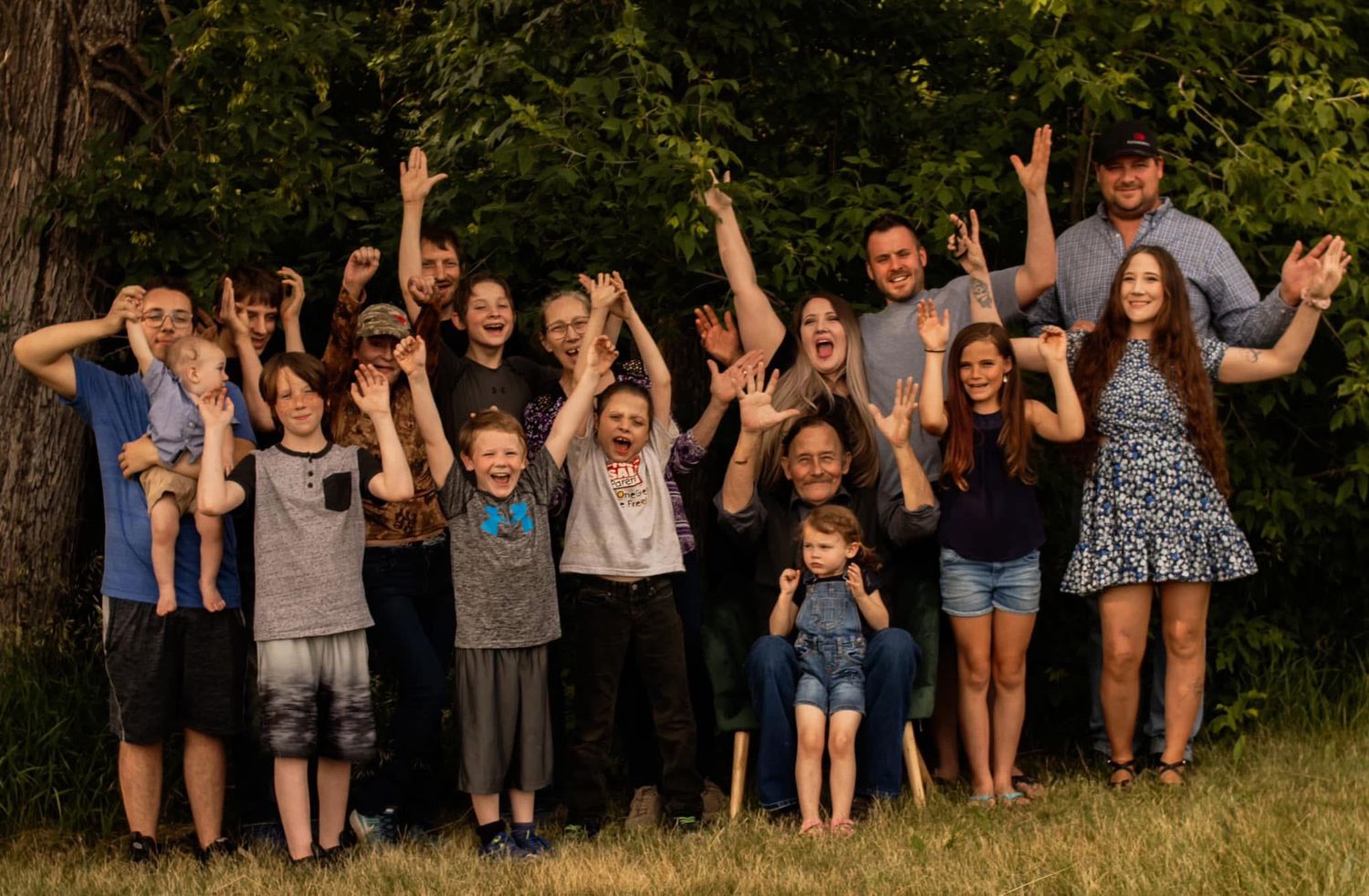 A joyful group photo of family members with raised arms celebrating outdoors.