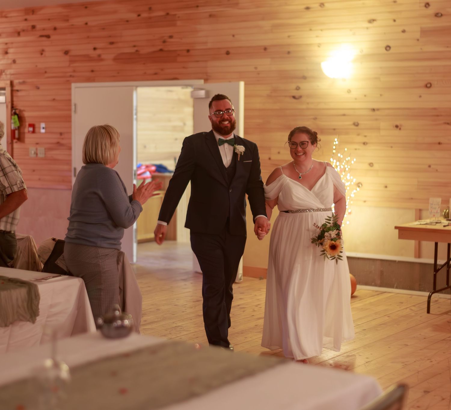 Wedding celebration in a cozy wood-lined reception hall with ambient lighting.