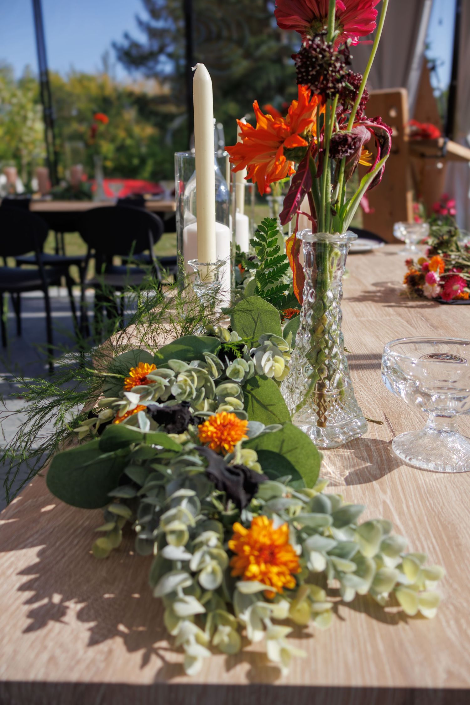 Table decorations featuring orange flowers and greenery for outdoor wedding reception.