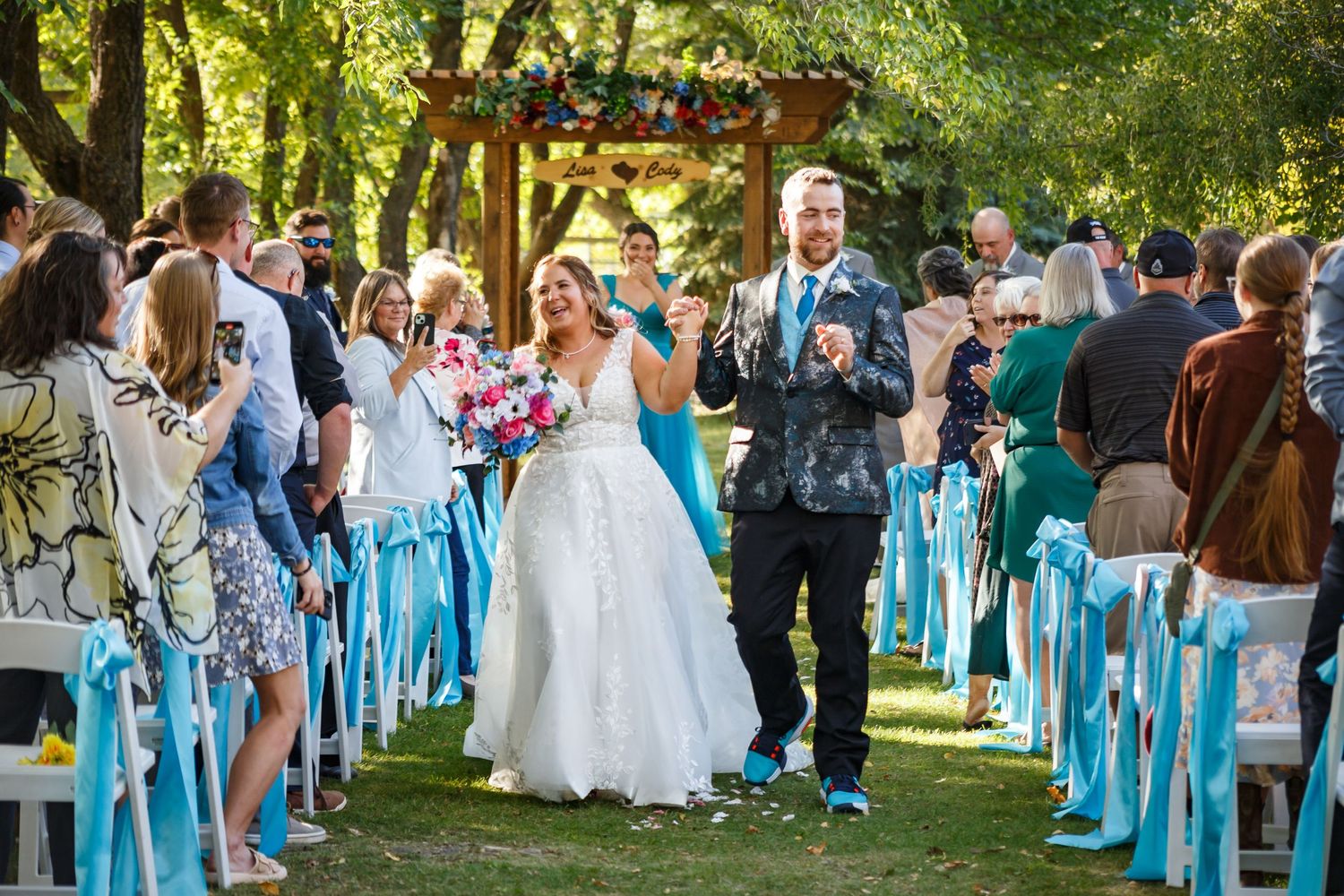 Wedding party in turquoise blue dresses gathered outdoors for celebration photos.