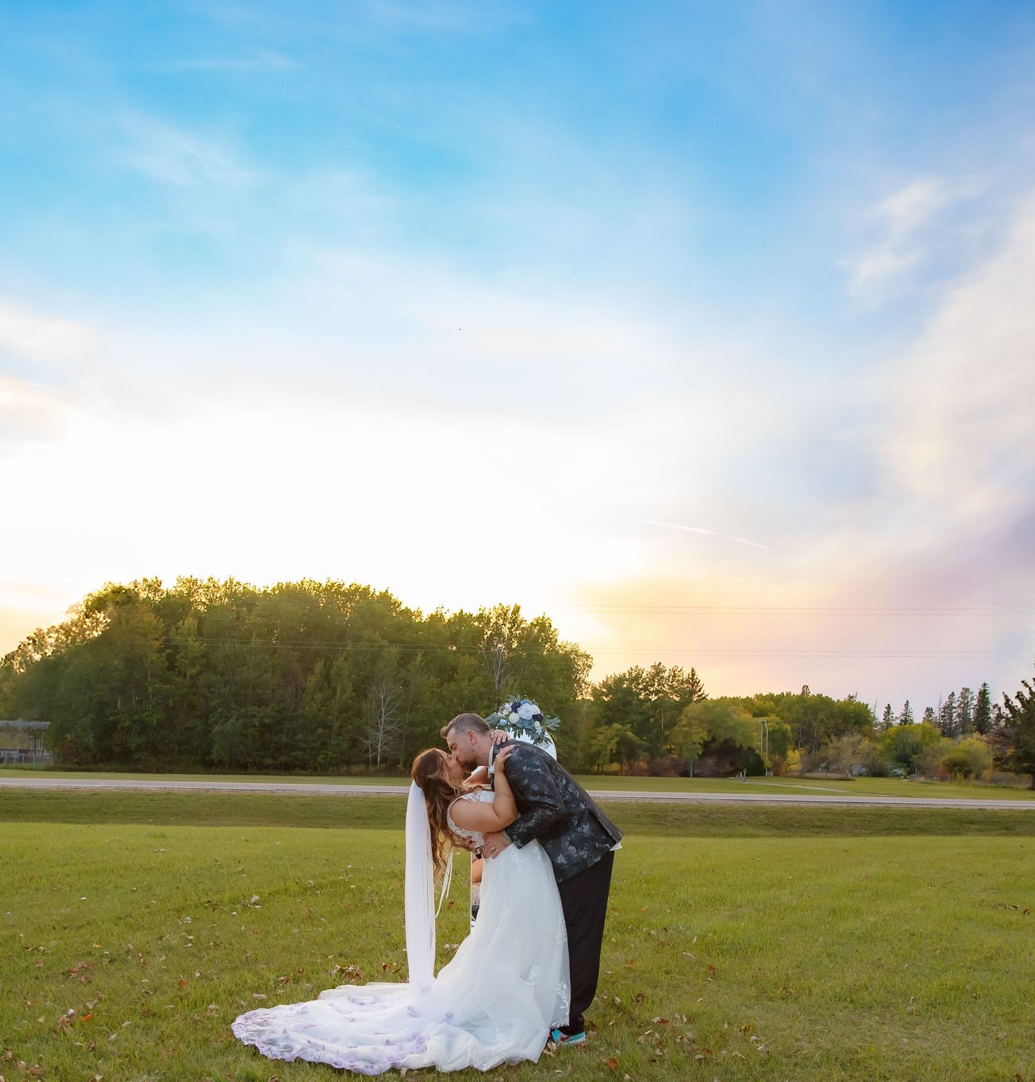 Sunset wedding portrait in an open field with trees on the horizon.