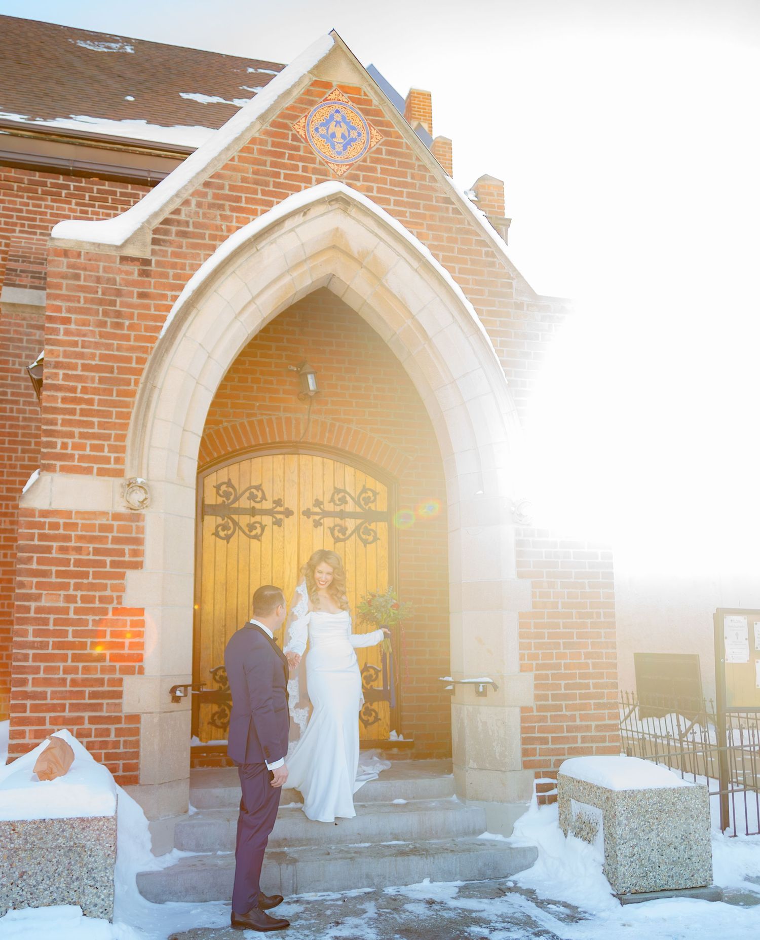 Wedding ceremony entrance at a brick church with Gothic arched doorway and bright sunlight.