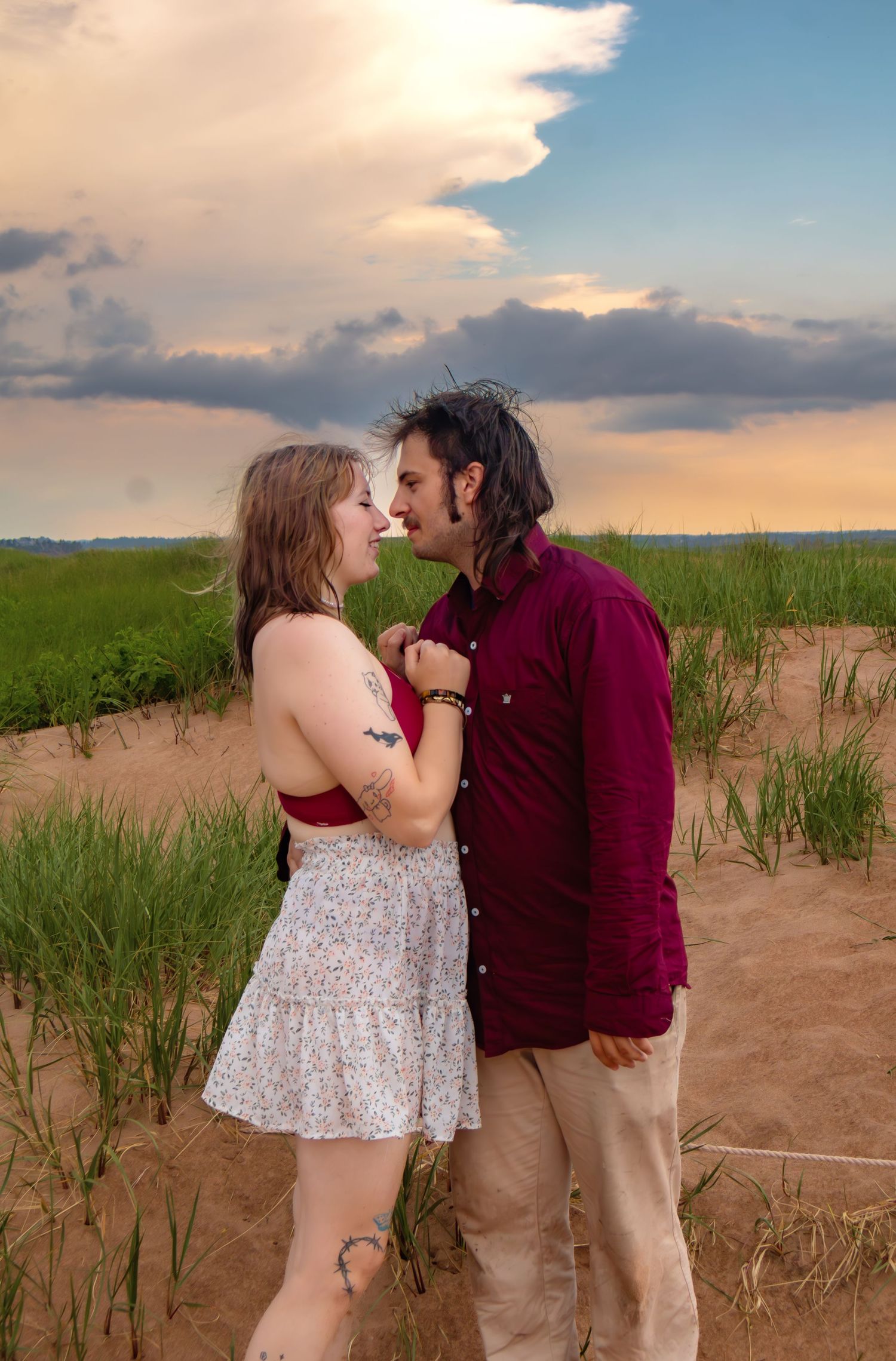 A couple shares a tender moment on a beach at sunset with golden clouds in the background.