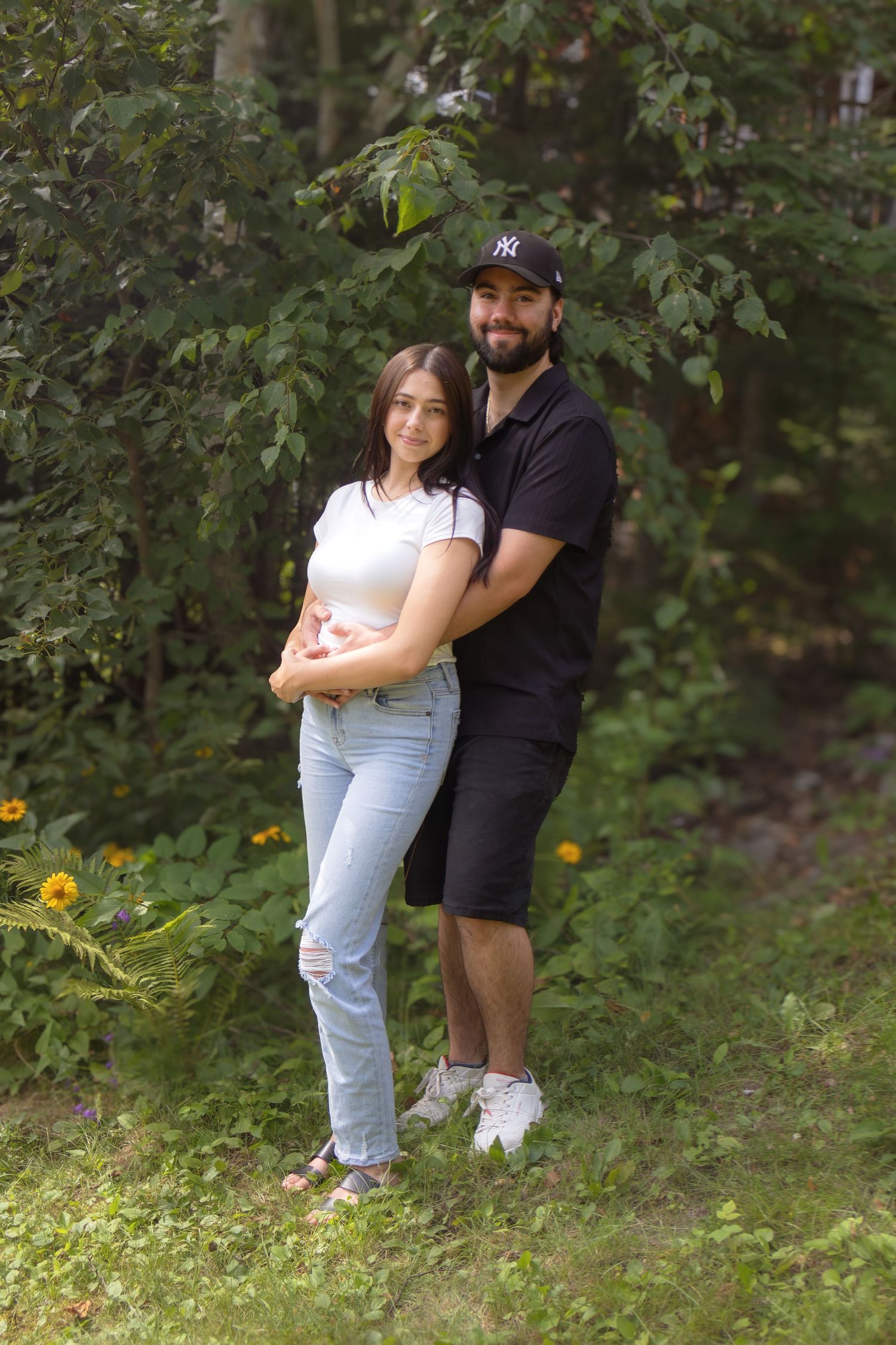 A couple embraces in a wooded outdoor setting with green foliage in the background.