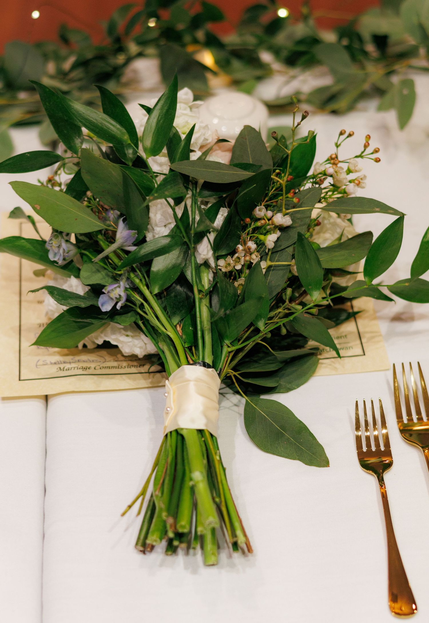 Fresh greenery and white floral bouquets arranged on a white tablecloth with gold cutlery.