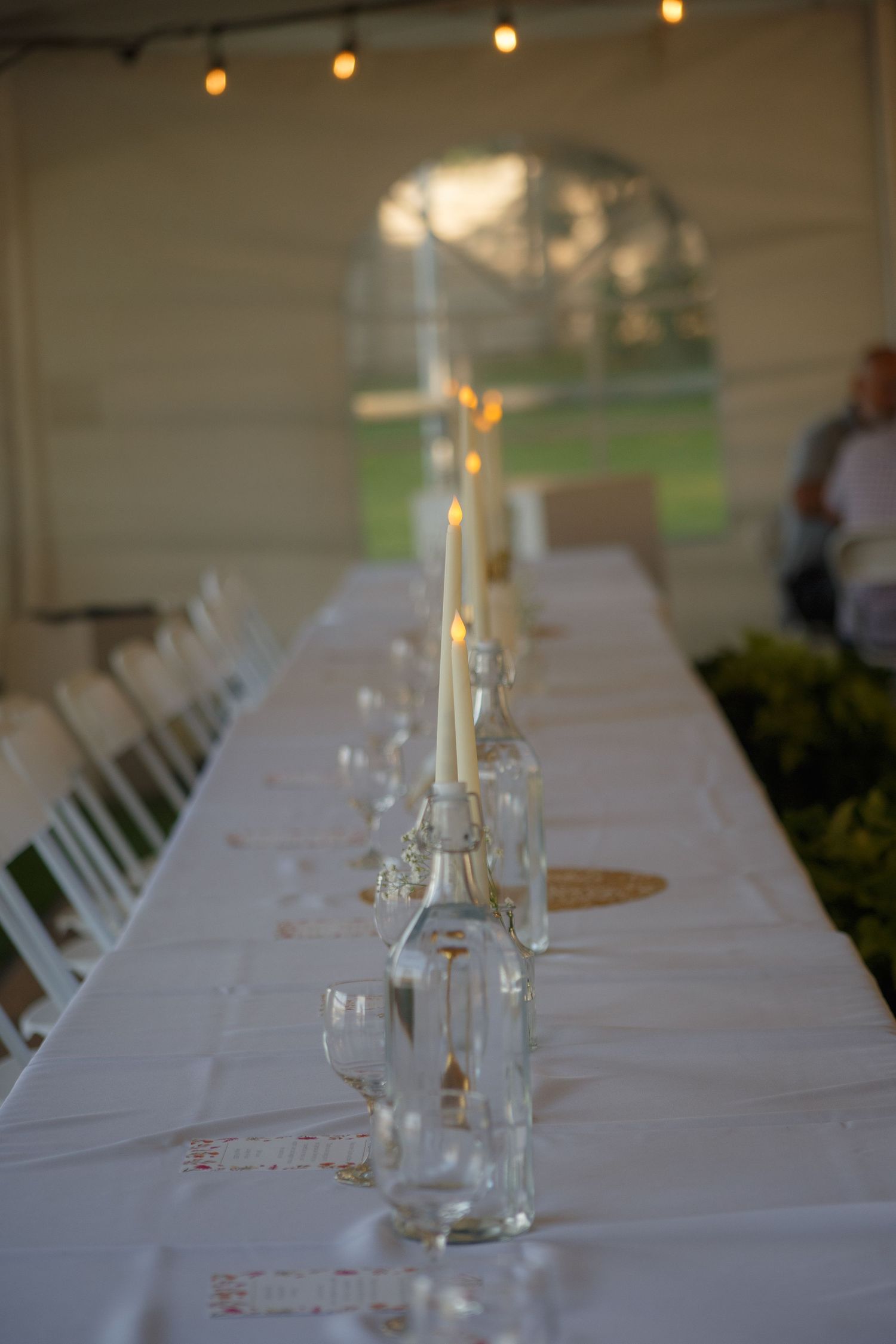 Elegant white tablescapes with glass bottles and candles for wedding reception.