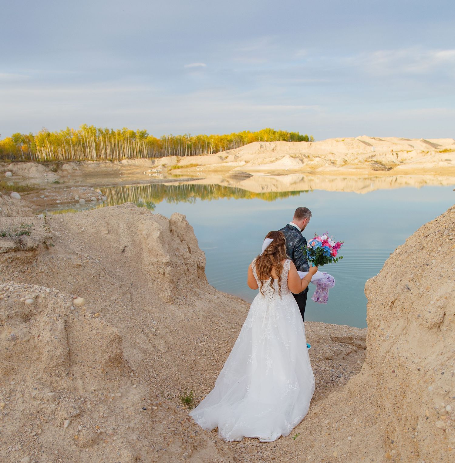 A couple poses for romantic wedding photos at sunset near sand dunes and a lake.