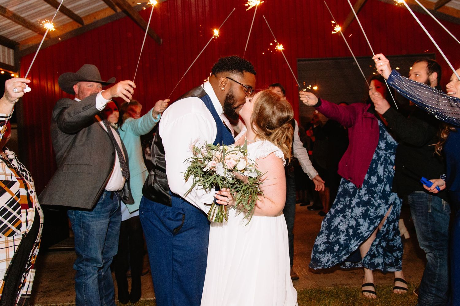 People dancing and celebrating at a lively indoor wedding reception with string lights overhead.