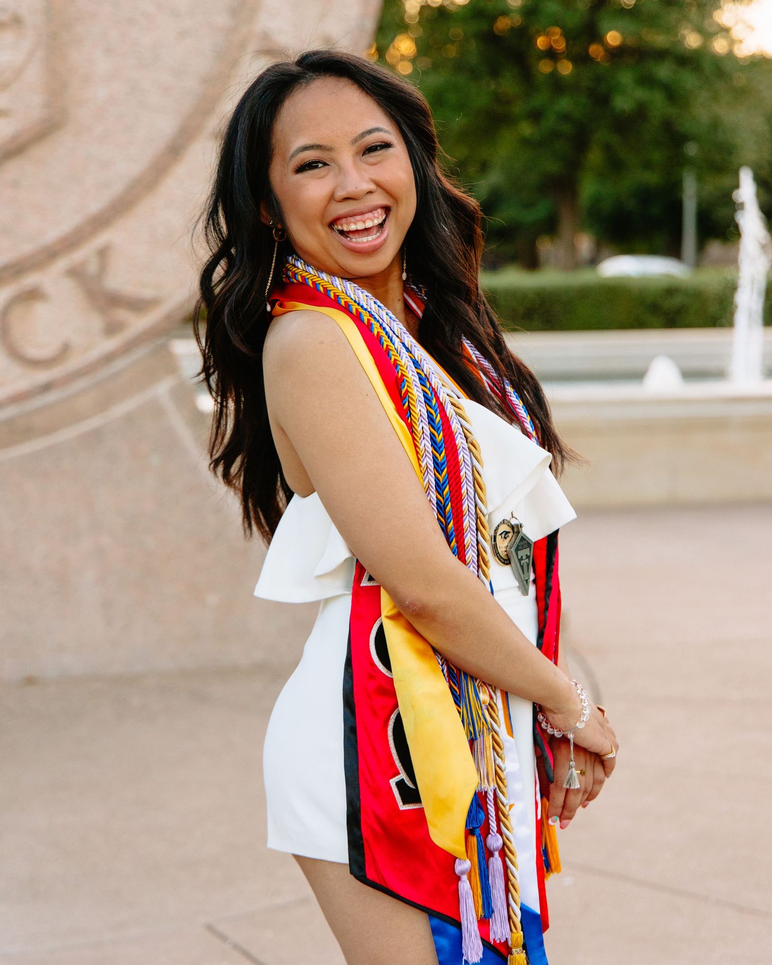 Graduate wearing colorful stoles and cords smiling during graduation photo session.