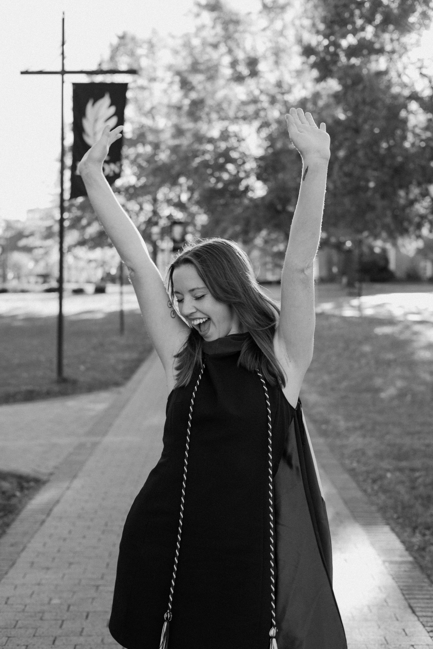 Graduate in black cap and gown celebrating with raised arms outdoors.