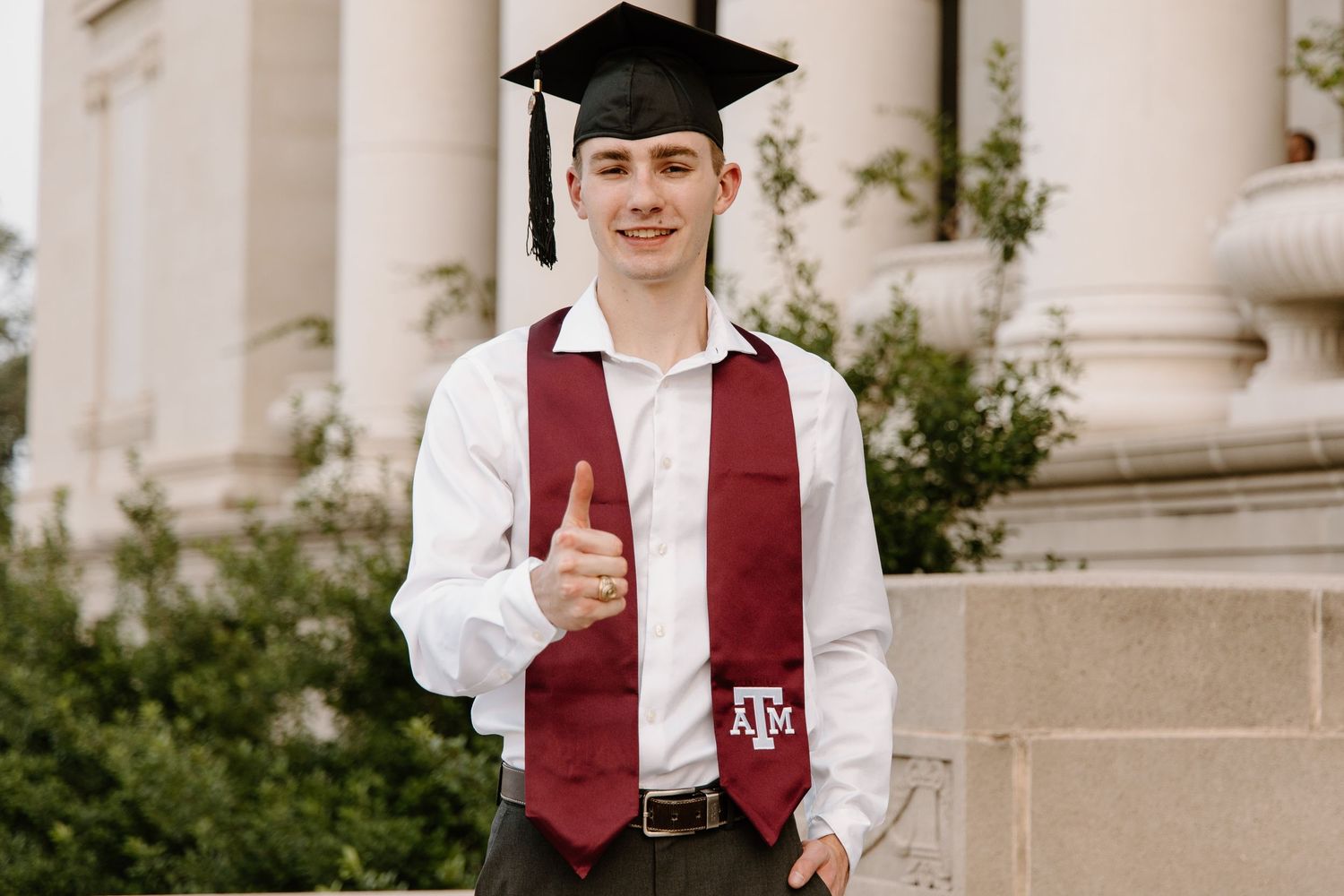 Graduate in white shirt and maroon stole standing near collegiate columns.