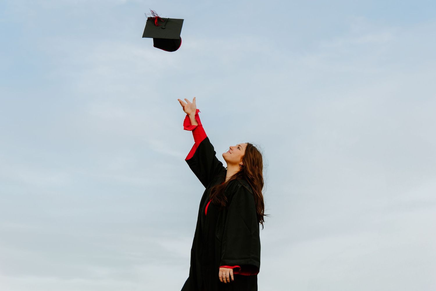 Texas Tech graduate throwing cap in the air against blue sky.