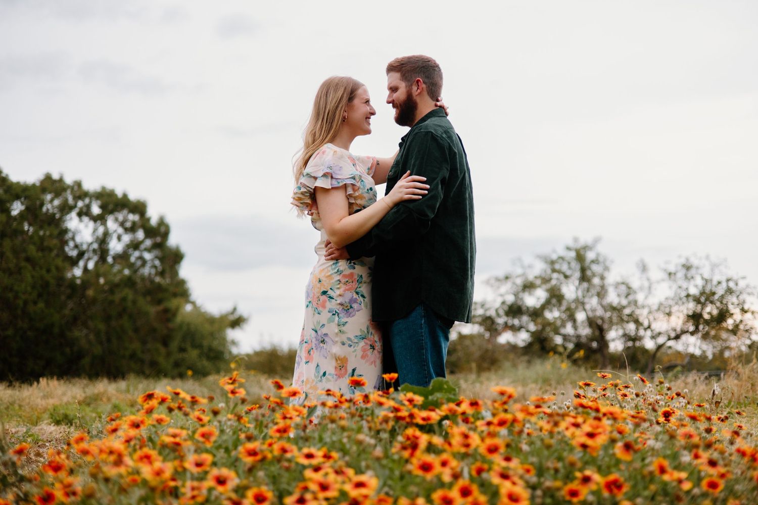 Couple embraces in a vibrant field of orange wildflowers during sunset.