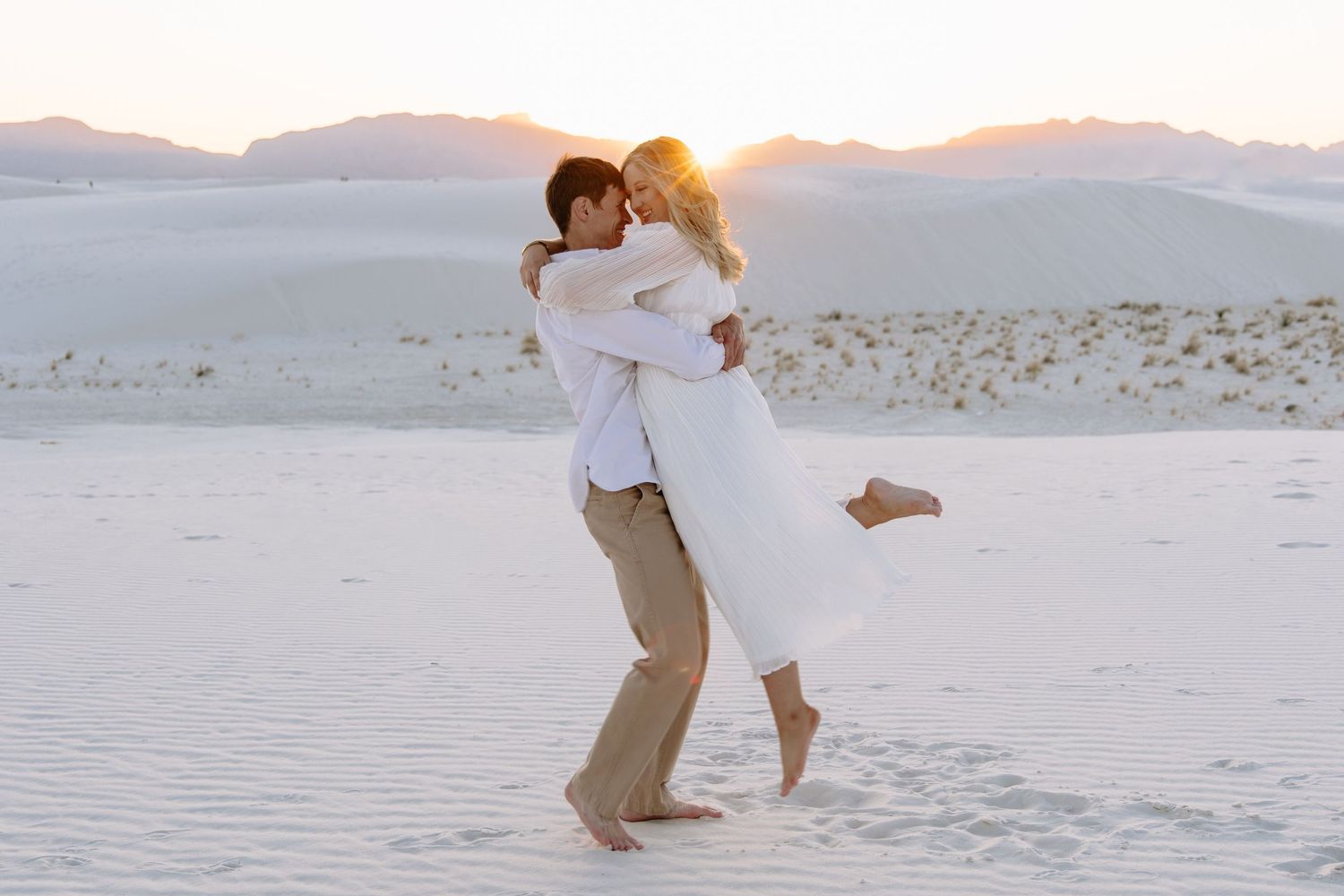 Couple dancing romantically on white sand beach at sunset.