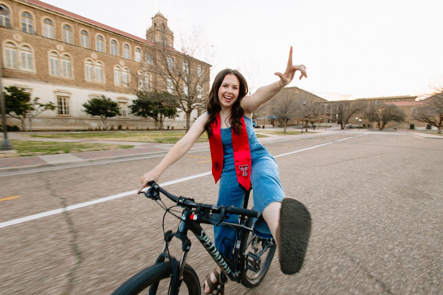 A couple rides bicycles together on a paved path outside a historic brick building.