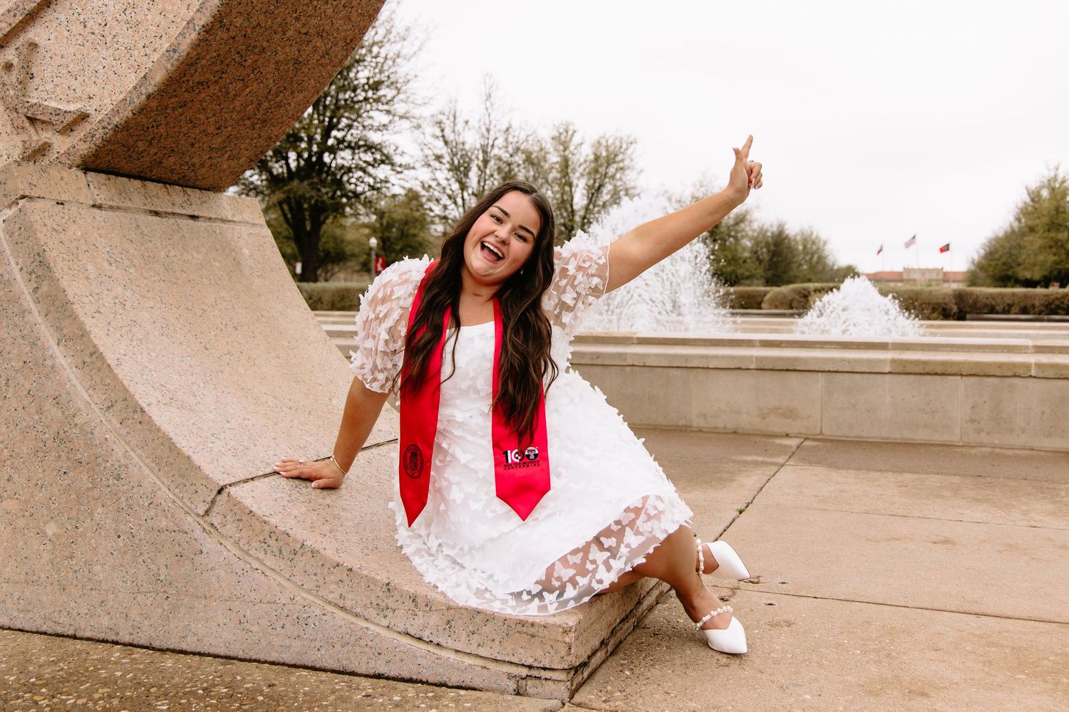 Playful graduation photoshoot in a columned walkway with dramatic architecture.