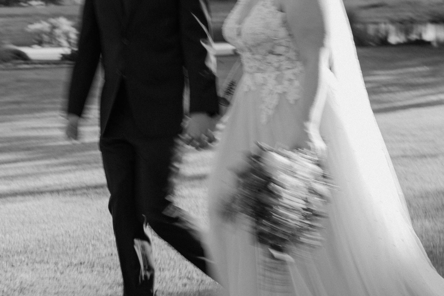 Motion blur black and white photo of couple walking with wedding bouquet.